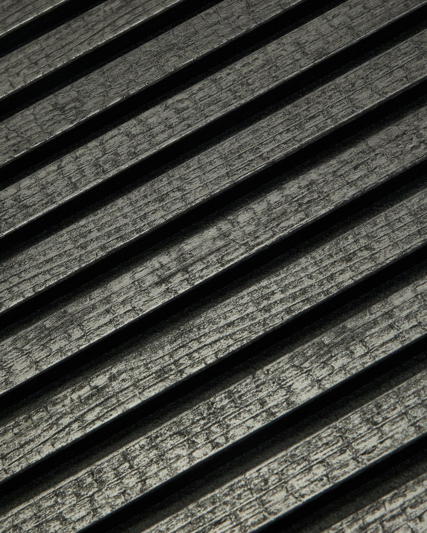 Primer plano de WoodUpp Rebel Akupanel en Charcoal (240x60 cm) que muestra black, lamas acústicas ranuradas dispuestas en diagonal para mejorar la absorción del sonido.