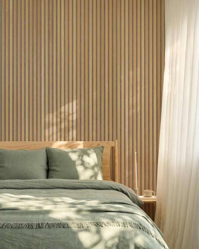 Dormitorio nórdico minimalista con una pared de roble WoodUpp Akupanel Panel acústico, ropa de cama verde salvia, estructura de cama de madera y cortinas blancas translúcidas.