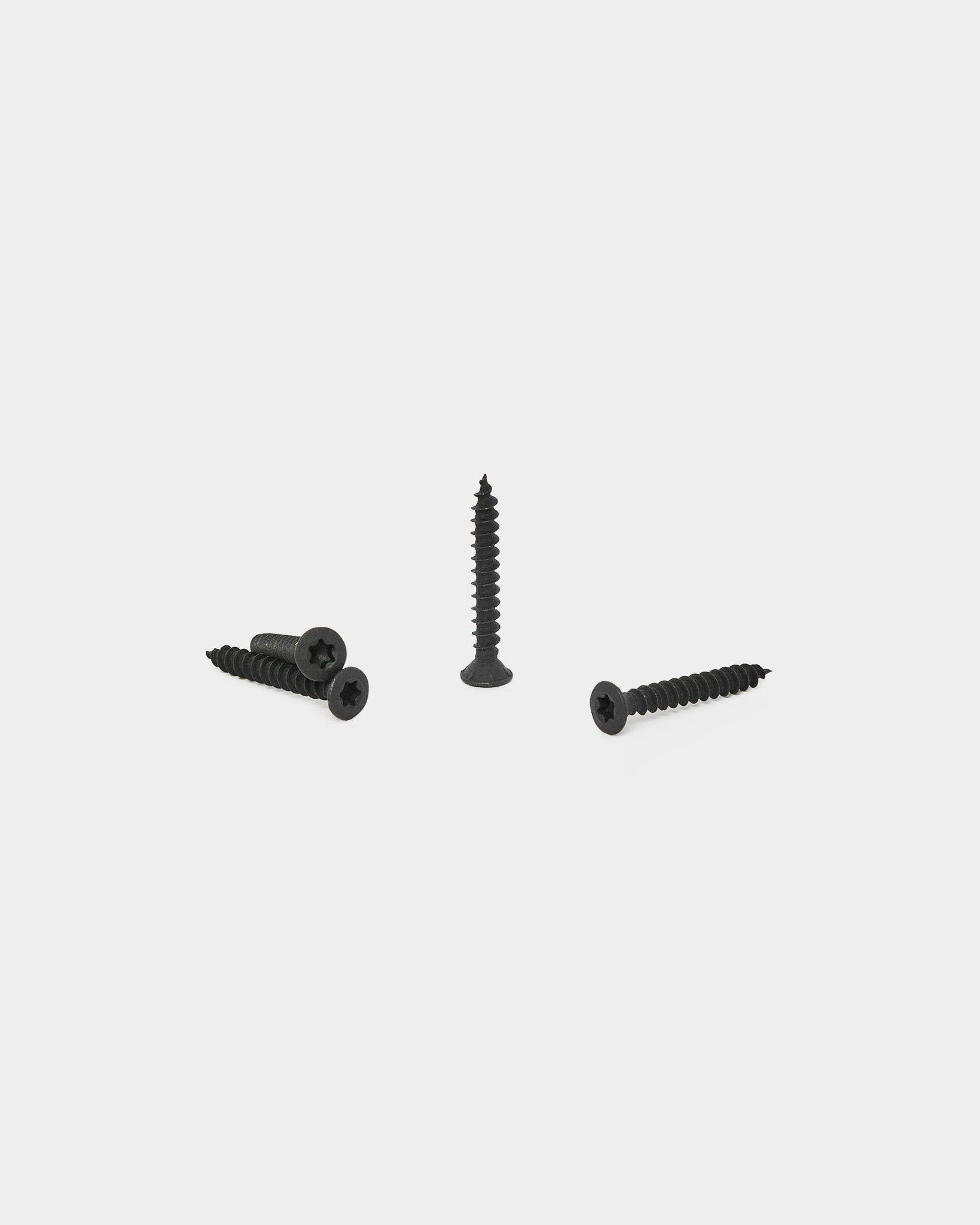 Cuatro tornillos de instalación WoodUpp black, tres colocados en horizontal y uno en vertical, presentados sobre un fondo blanco para la instalación de Akupanel Panel acústico.