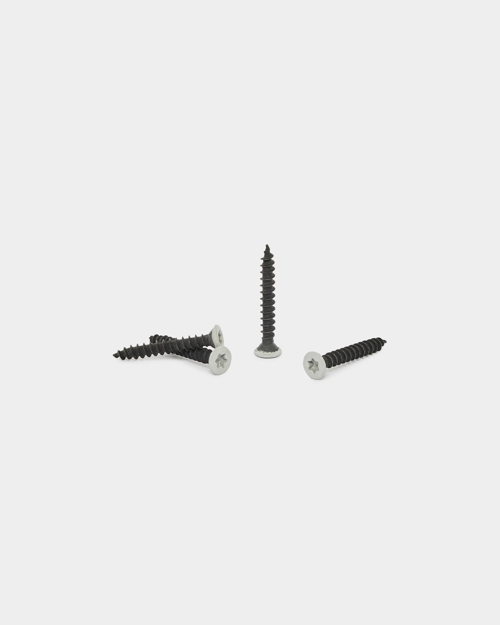 Cuatro tornillos WoodUpp grey del set de productos de instalación (100 uds.) sobre un fondo blanco liso; tres están horizontal y uno está de pie.