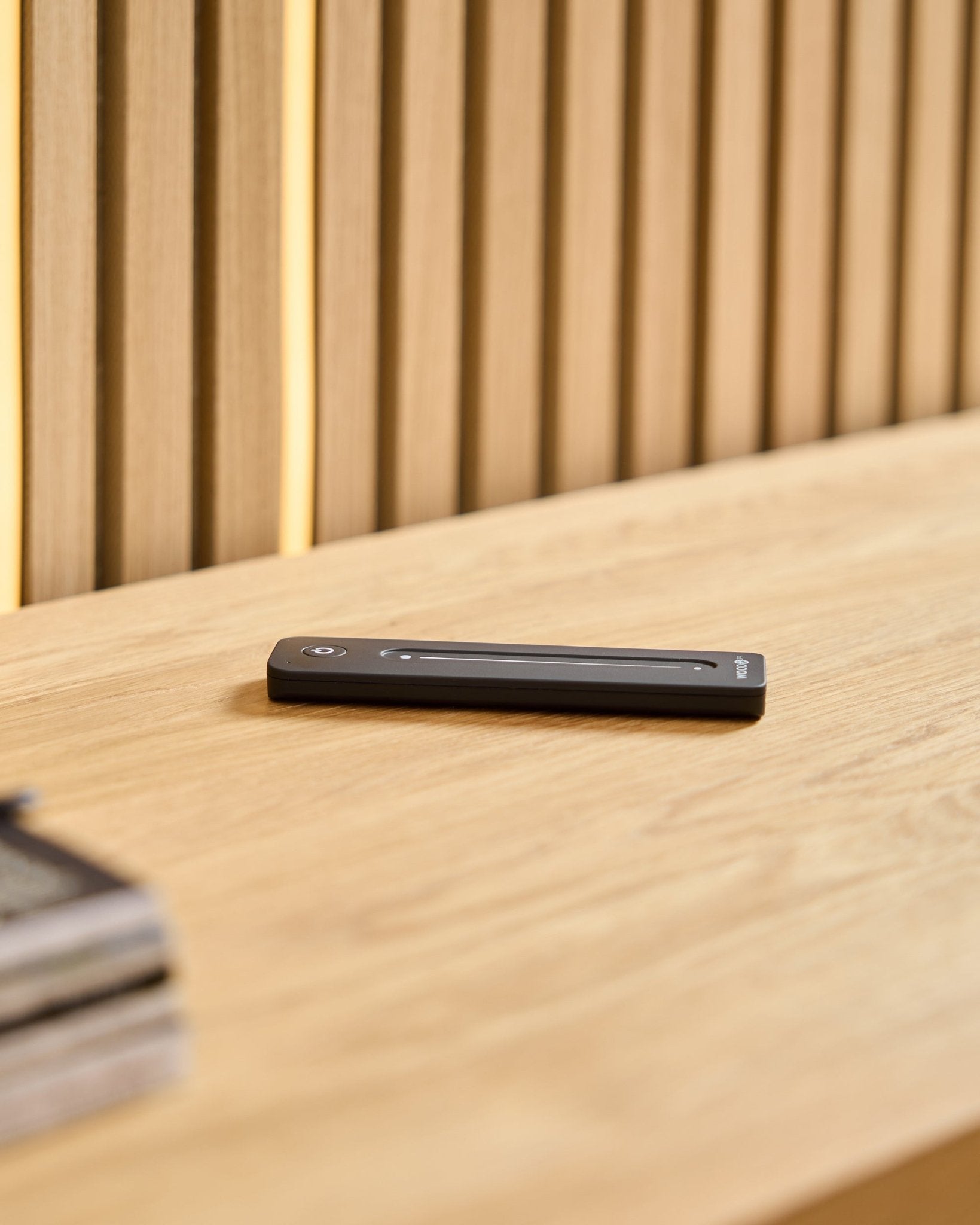 Un mando LED black WoodUpp Lumi sobre una superficie de madera clara, con un fondo de paneles acústicos de madera con listones.