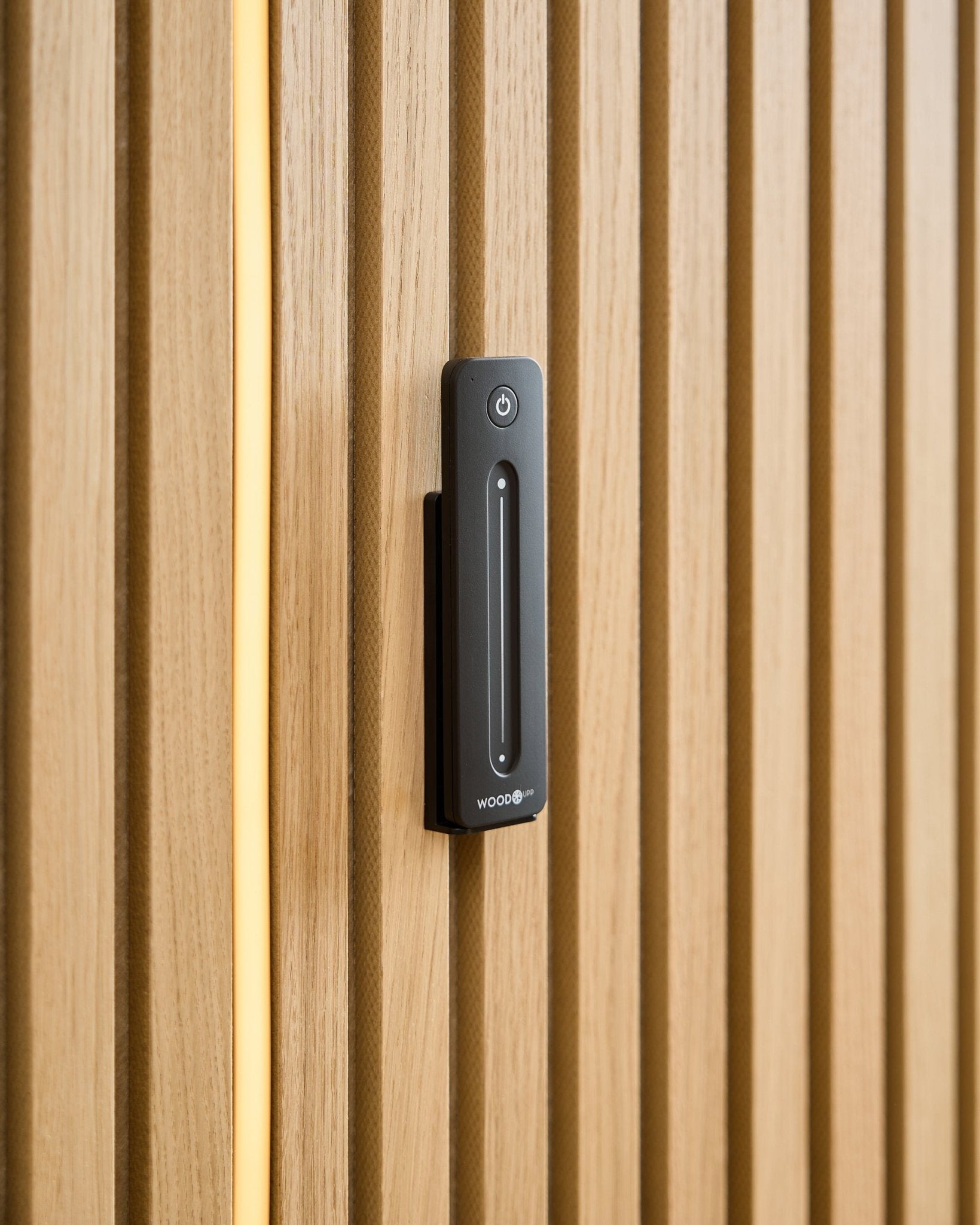 Un WoodUpp Lumi | Remote / LED Striplight está instalado en un Panel acústico de madera clara, con un cable amarillo visible detrás de los listones de madera.