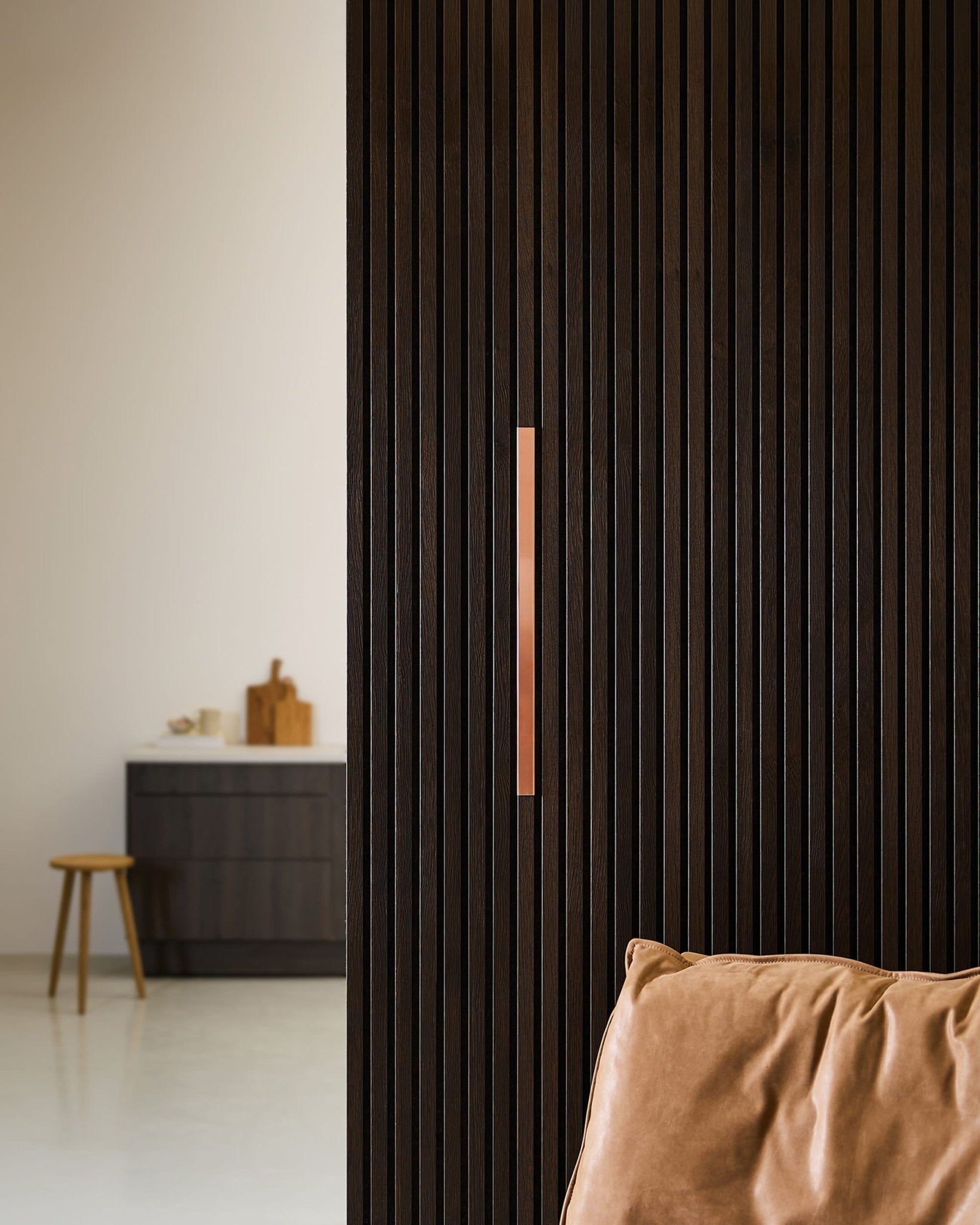 Cocina minimalista con un panel WoodUpp Liva | Cover / Copper en una pared de 60 cm, silla de cuero color tostado, taburete y encimera.