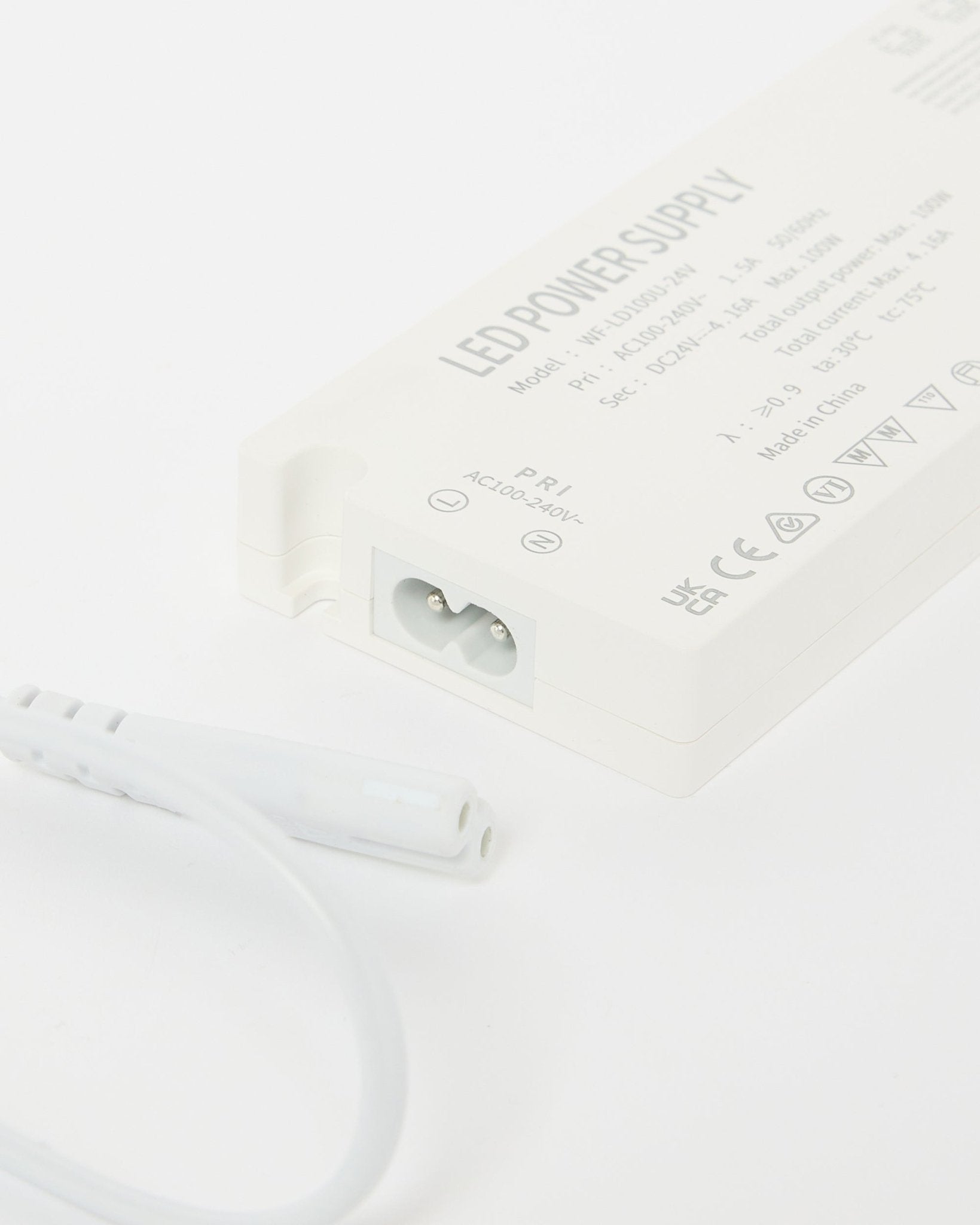 Primer plano de una fuente de alimentación para tiras LED WoodUpp Lumi de beige (240 cm), mostrando detalles técnicos, con un cable al lado, diseñada para instalaciones nórdicas Panel acústico.