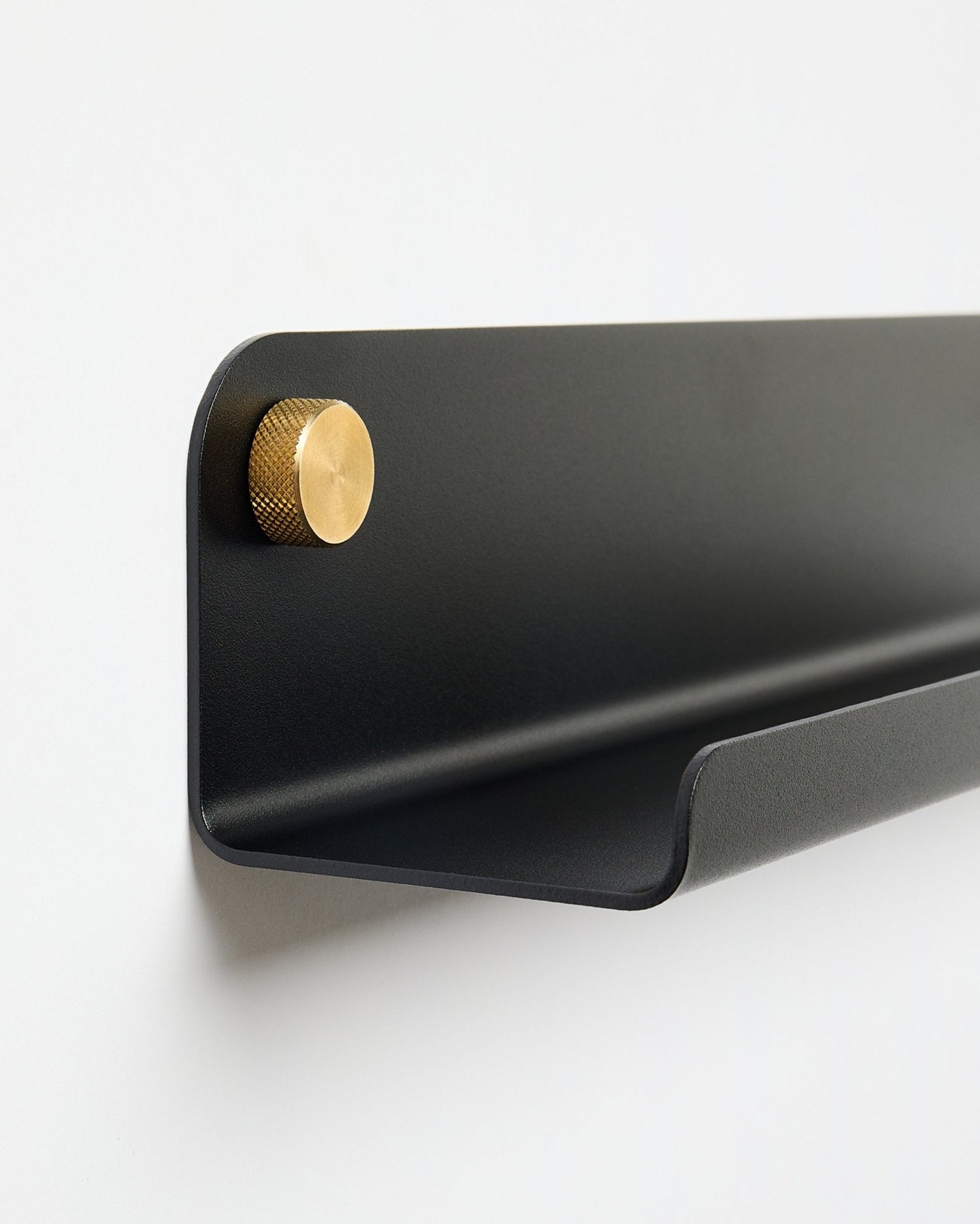 La Norr | Narrow Shelf en black (115.9 cm), con un único pomo dorado a la izquierda, de WoodUpp, montada en una pared blanca lisa.