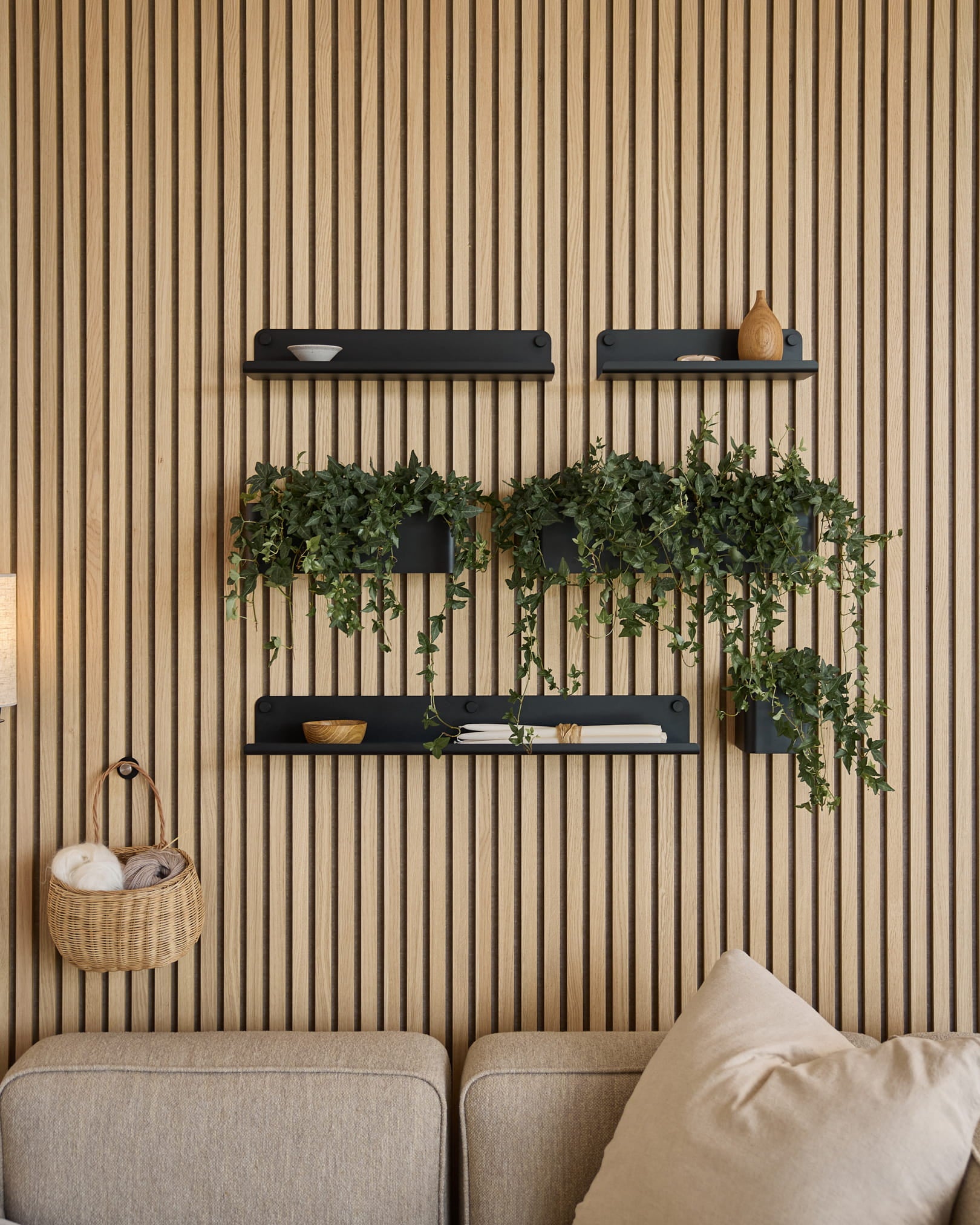 Salón moderno con un panel acústico nórdico de listones, estantes black, plantas colgantes en la Plant Box Norr de WoodUpp (35.9 cm, Black) y un sofá beige.