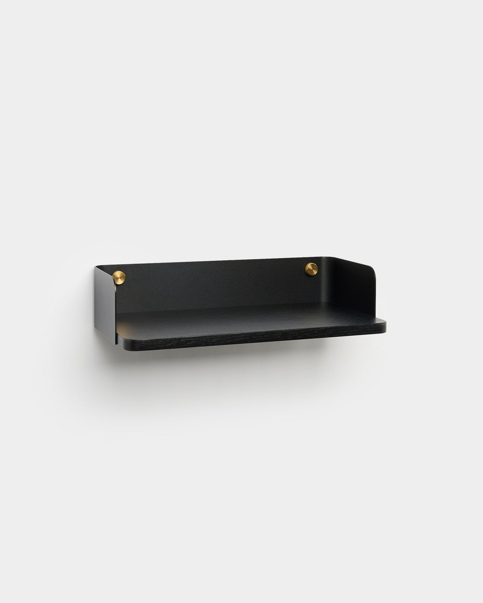 La estantería Linn de WoodUpp, con un acabado minimalista black y tornillos de montaje brass, está instalada en una pared gris claro y encaja con el diseño interior nórdico.