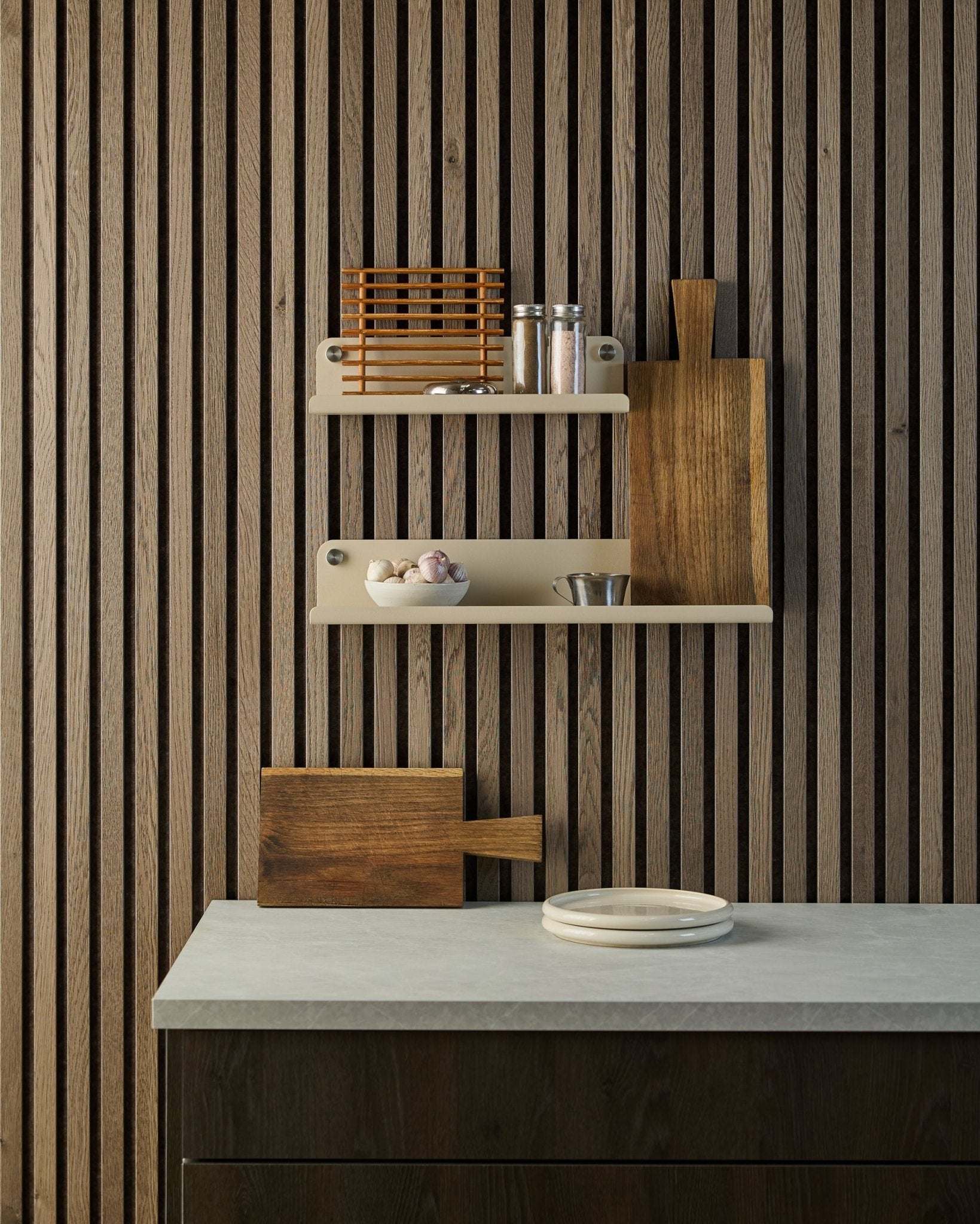 Cocina minimalista con panel acústico de listones de madera nórdica Akupanel, estantes abiertos con especias y cuencos, y encimera con platos blancos y una tabla de cortar.