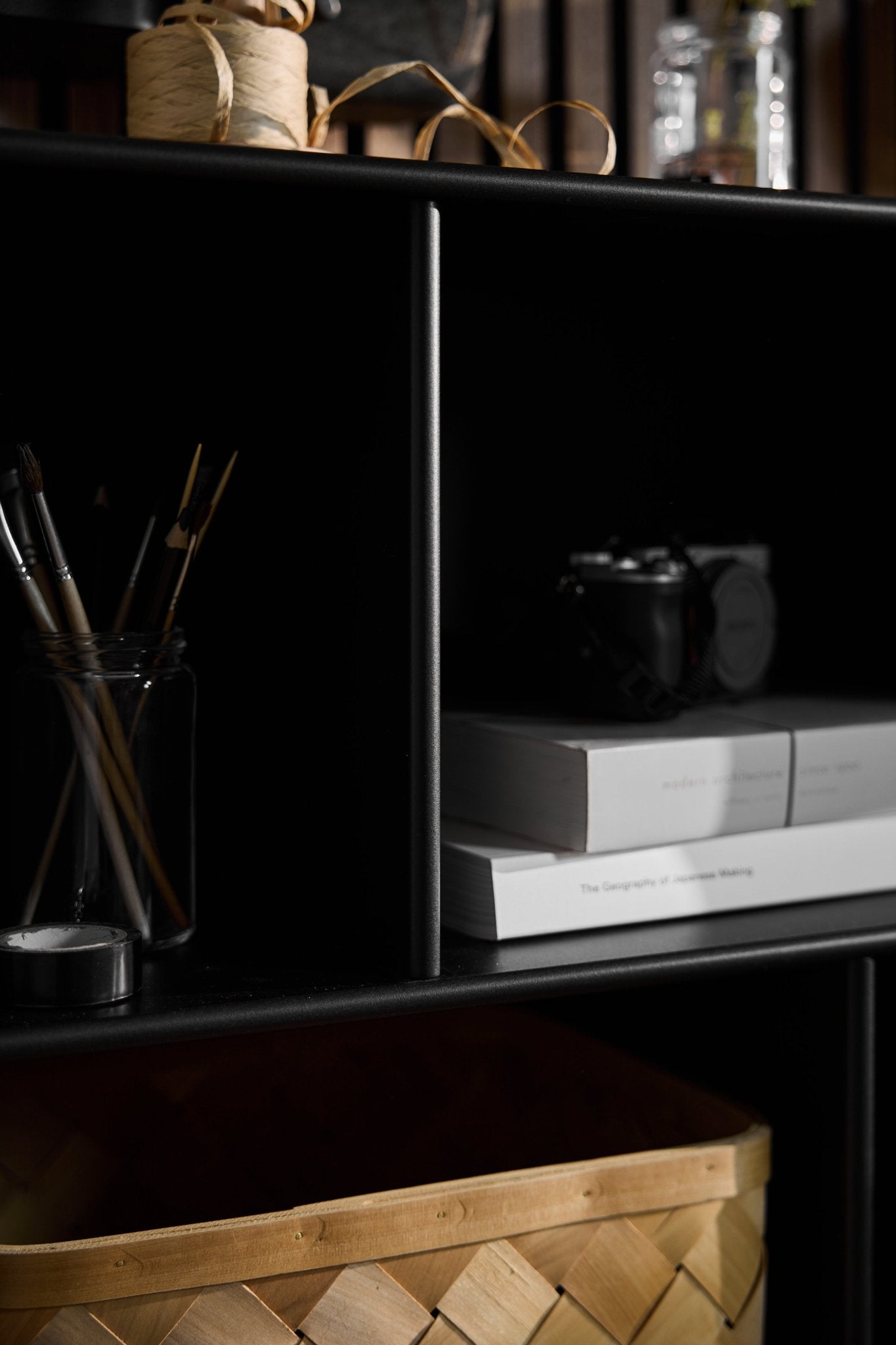 Armario abierto «Arka» de WoodUpp, de color negro, con tarros, libros, una cámara, una cesta y cordel dispuestos en los estantes de una habitación de estilo nórdico con una iluminación suave.