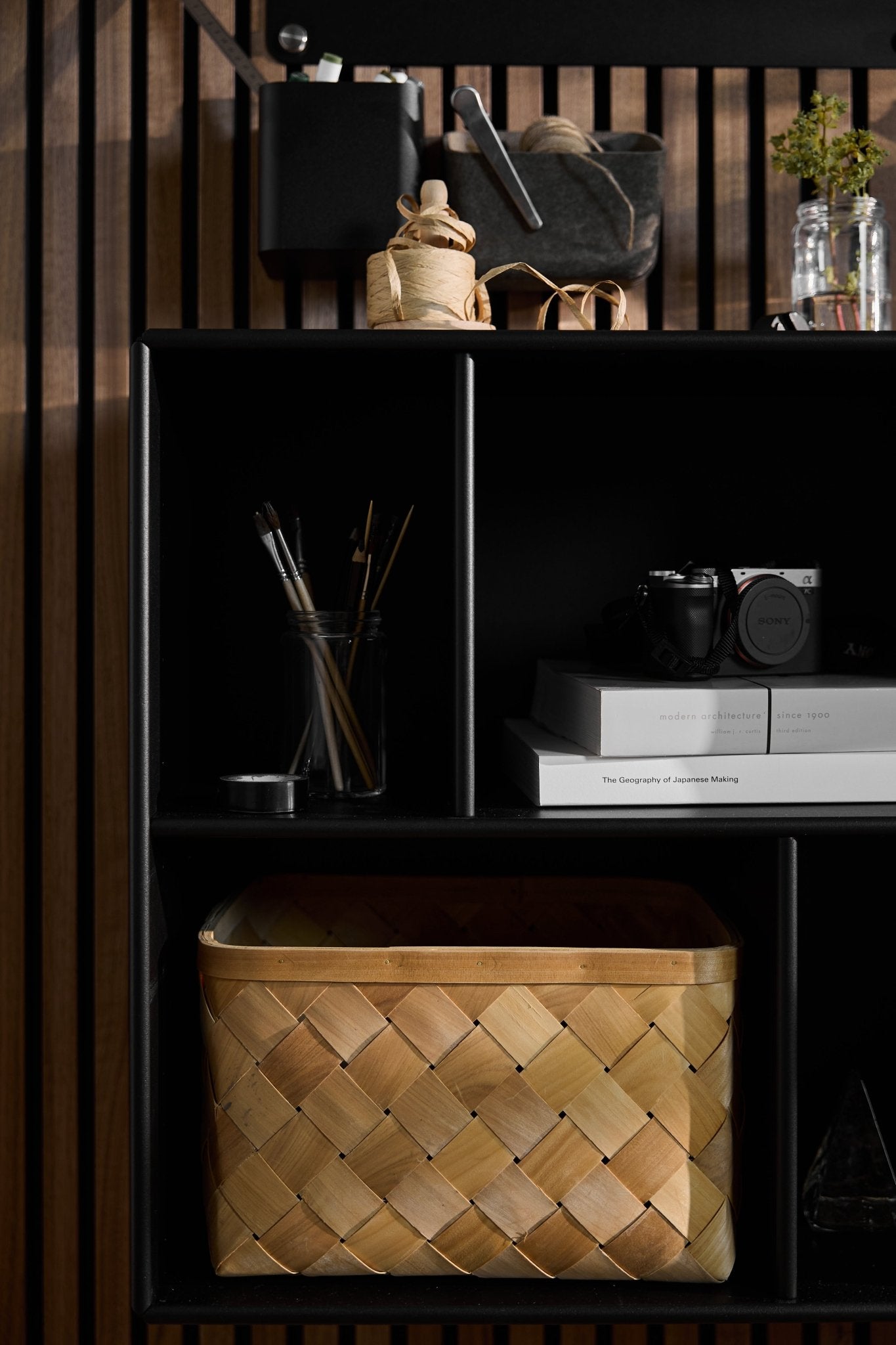 Arka | El armario abierto «Black» de WoodUpp alberga materiales de arte, libros, una cámara y una cesta, con un fondo de paneles acústicos de lamas Akupanel de estilo nórdico.