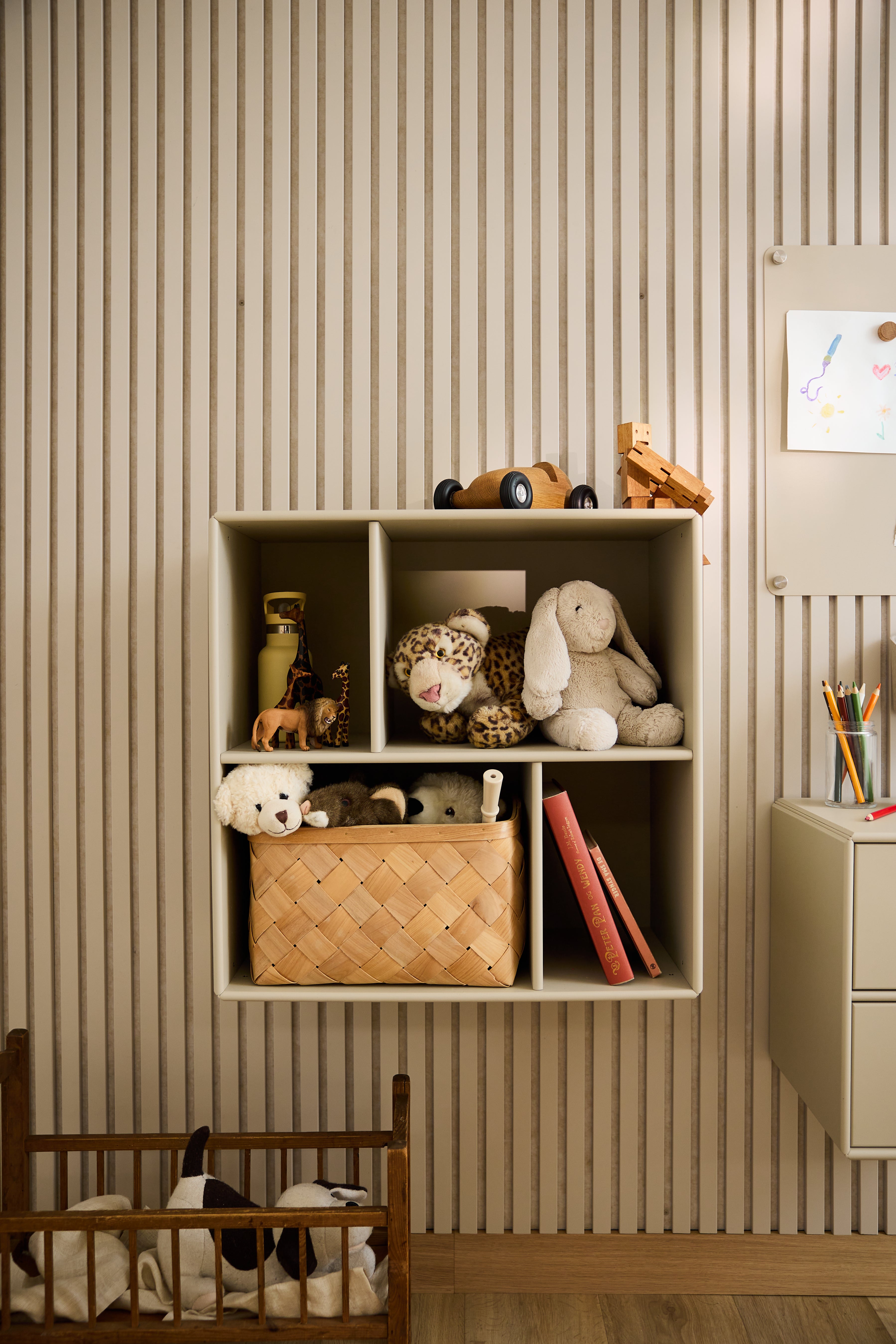 El armario abierto Arka de WoodUpp, en color beige y con juguetes y libros, destaca sobre el papel pintado a rayas de una habitación infantil y es un ejemplo del diseño nórdico minimalista.