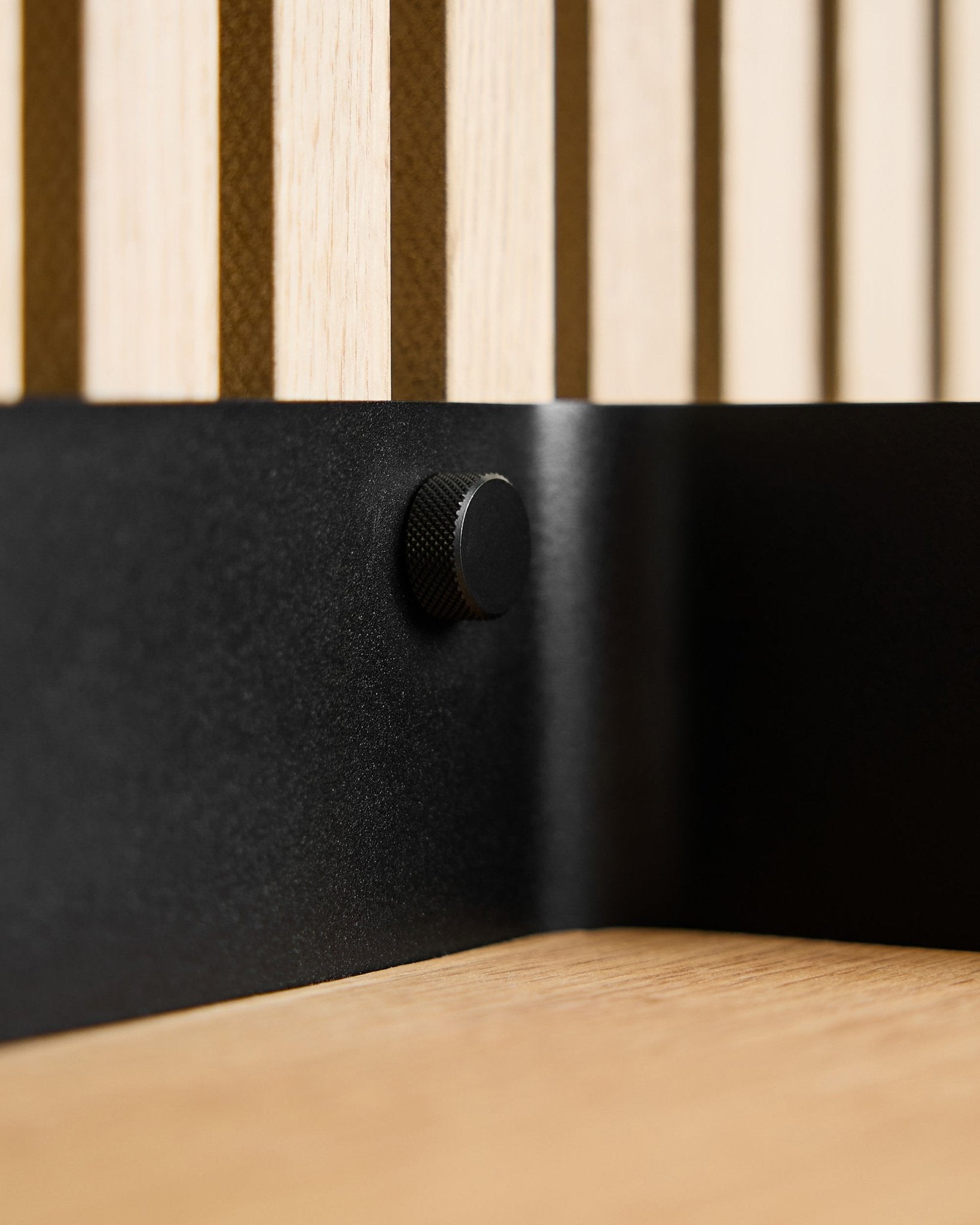 Primer plano de dos tornillos Finger WoodUpp black (M5x10 mm, 20x8.8) con tornillos brass, colocados sobre un panel acústico de listones de madera nórdica y una superficie de madera clara.