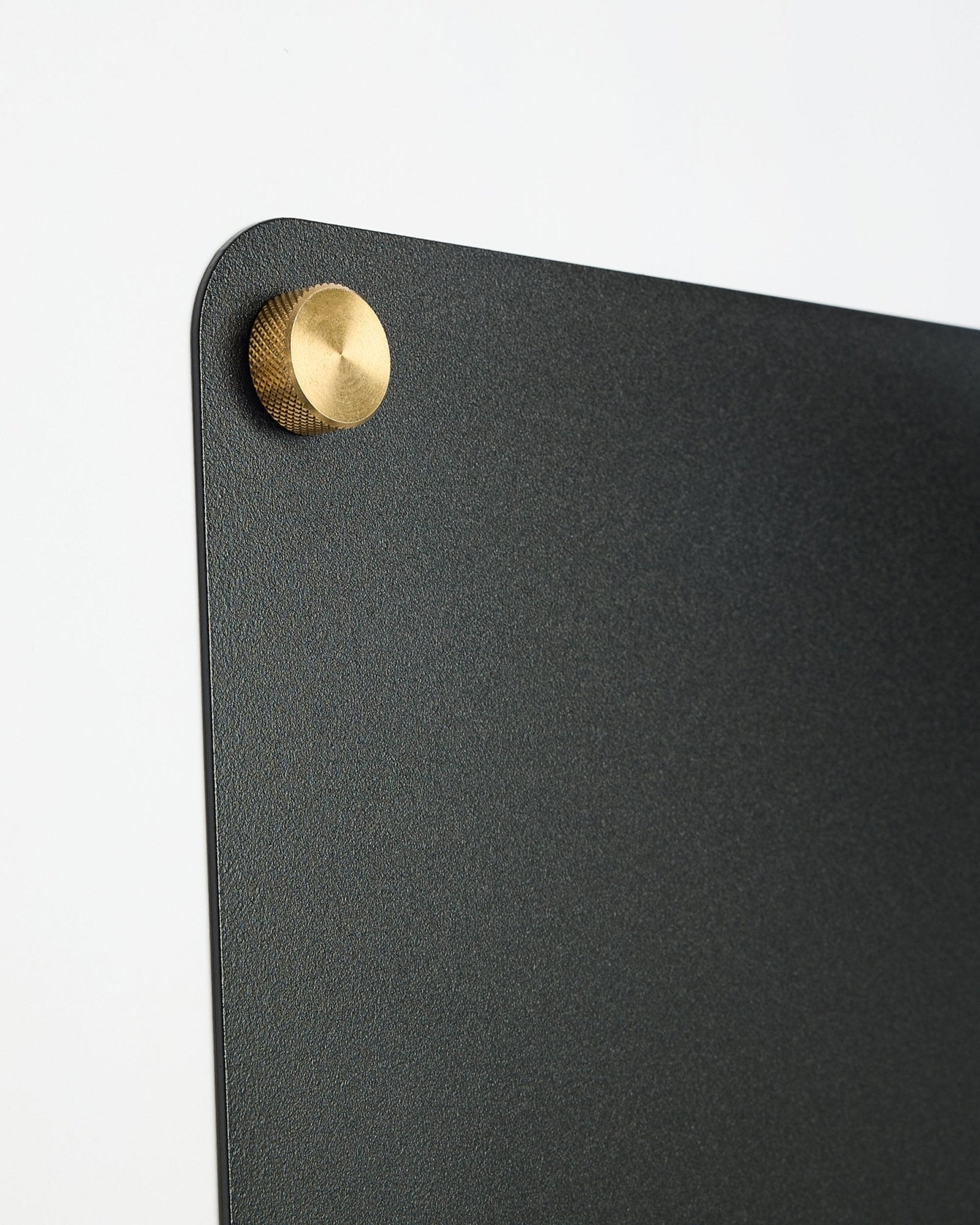 Primer plano de un large black Norr tablero magnético de WoodUpp, parte de la colección CREATE, con un fijador metálico redondo en oro colored en la esquina superior.