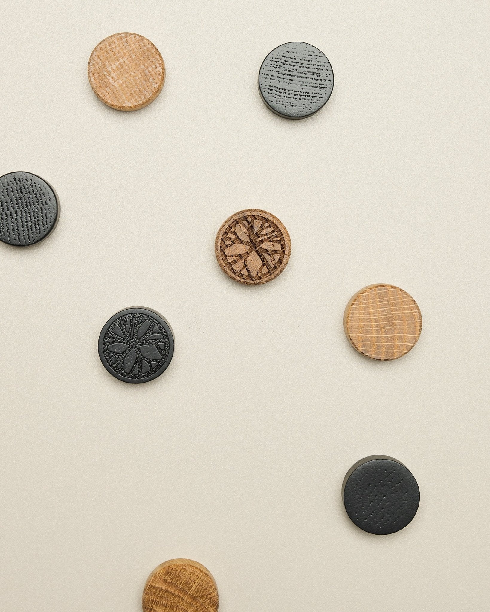 El set de imanes Norr de WoodUpp incluye cuatro discos con motivos de natural oak y black, colocados con cuidado sobre una superficie clara de beige; accesorio para Akupanel.