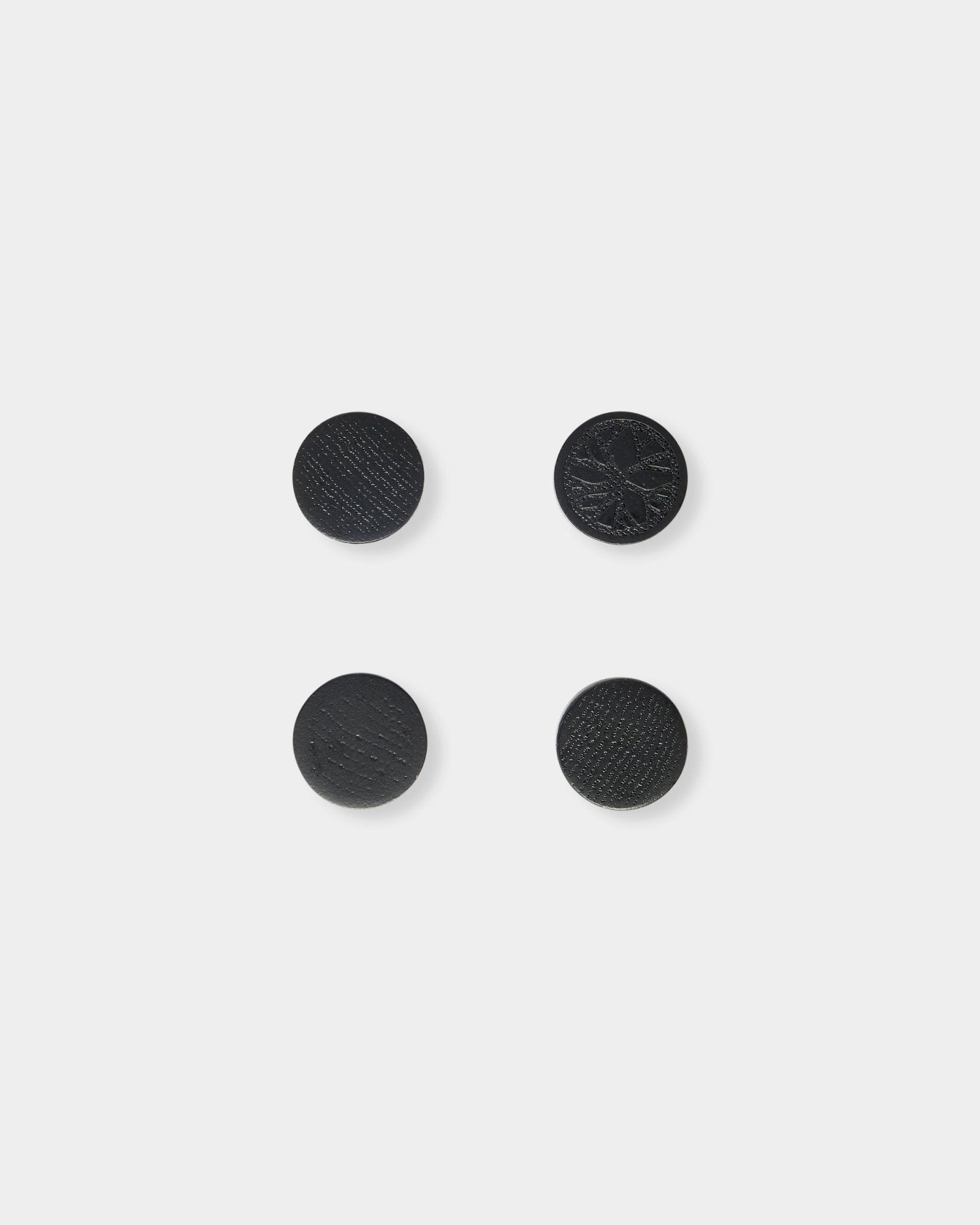 Juego de cuatro imanes Norr black oak de WoodUpp, colocados con cuidado en forma de cuadrado sobre un fondo liso gris claro.