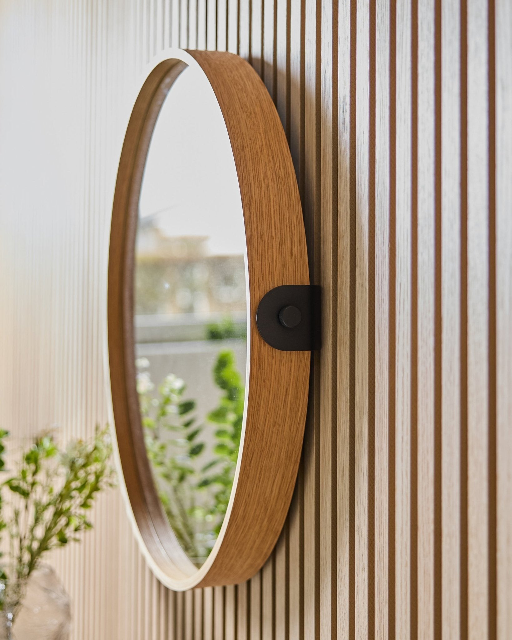 Linn | Mirror / Natural Oak de WoodUpp montado en una pared Panel acústico de rayas, reflejando vegetación y luz natural de una ventana cercana.