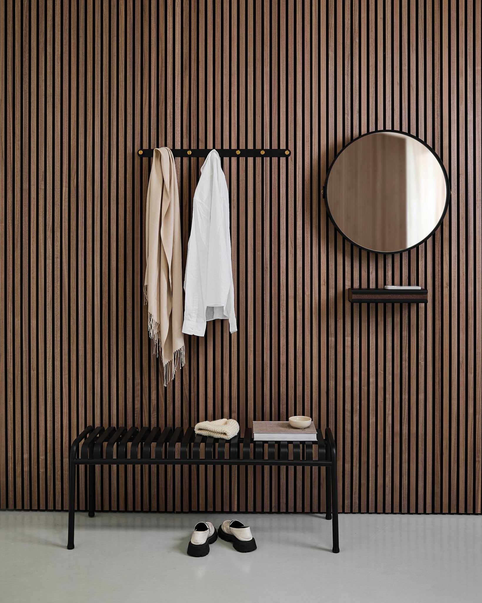 Recibidor minimalista con un WoodUpp Linn | Mirror en Black Oak, panel acústico nórdico de listones, banco, estante, abrigo y bufanda colgados, y zapatos en el suelo.