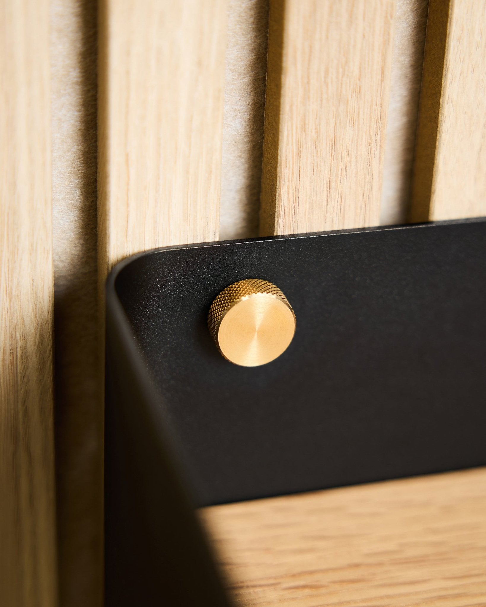 Primer plano de dos tornillos moleteados WoodUpp brass (M5x10 mm, 20x8.8), fijados a un soporte black montado sobre una superficie Panel acústico de madera nórdica clara.