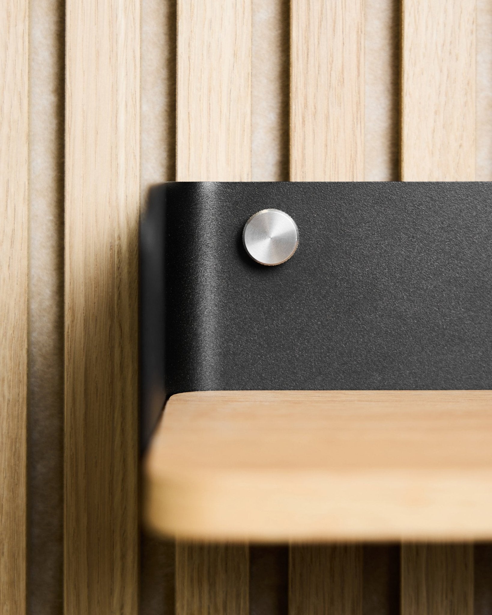Primer plano de una balda de madera clara con soporte metálico black, montada con tornillos de apriete manual WoodUpp (M5x10 mm, acero inoxidable steel), combinada con Nordic Panel acústico.