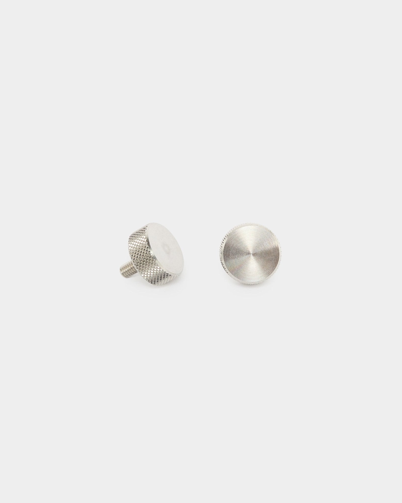 Dos tornillos de apriete manual WoodUpp de acero inoxidable steel (M5x10mm, 20x8.8), accesorios para paneles acústicos Akupanel, colocados en vertical y en plano sobre un fondo blanco liso.