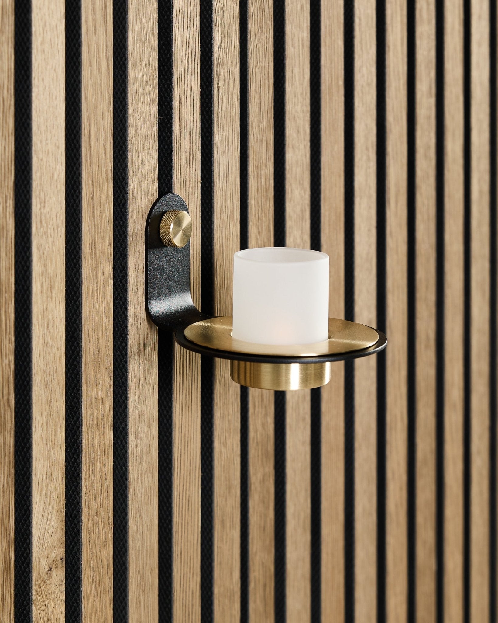 El portavelas Norr en black y brass de WoodUpp está montado sobre un panel acústico de madera Akupanel de estilo nórdico con lamas black vertical.