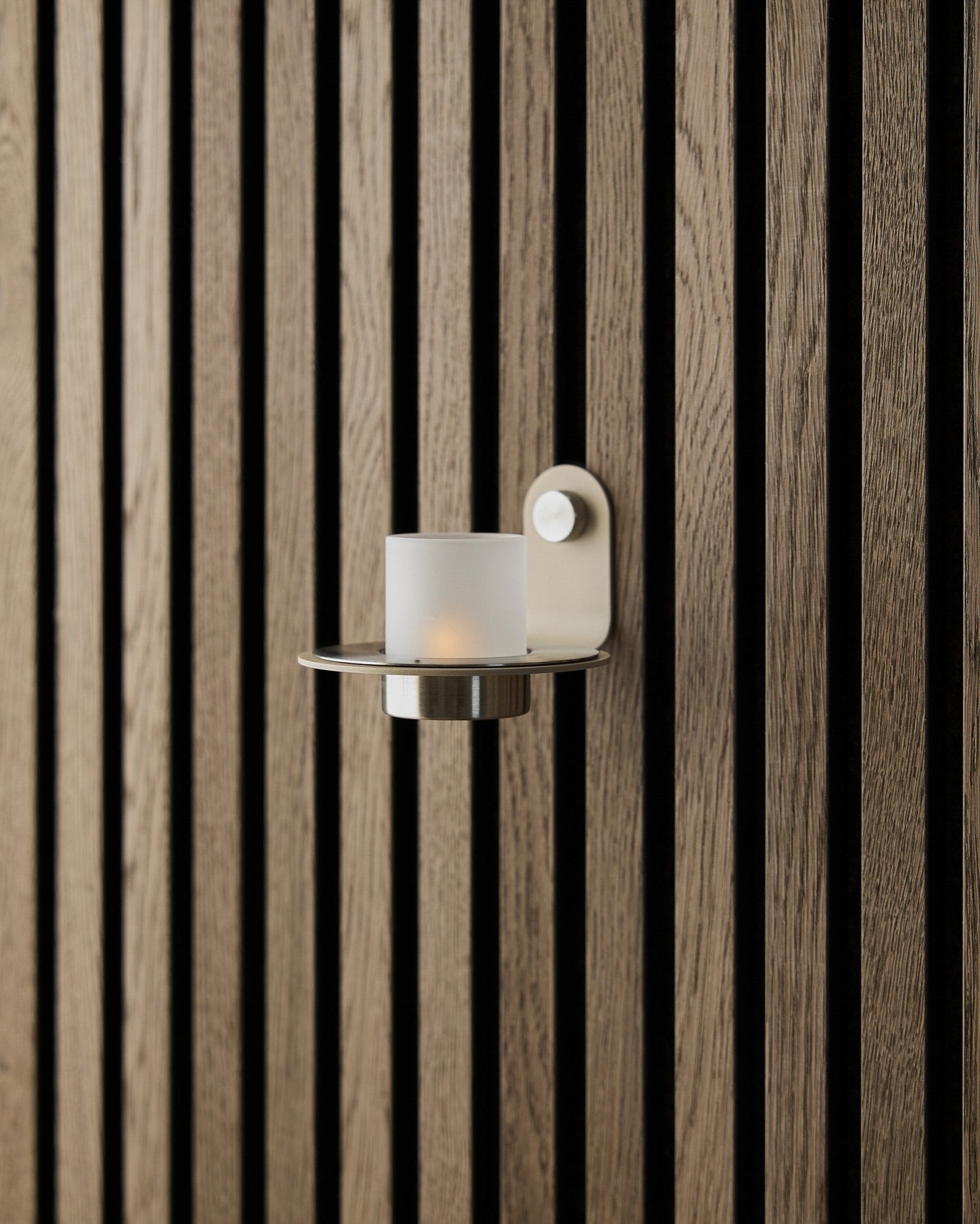 El portavelas Norr en steel inoxidable beige de WoodUpp, expuesto sobre una pared con Panel acústico Akupanel beige.