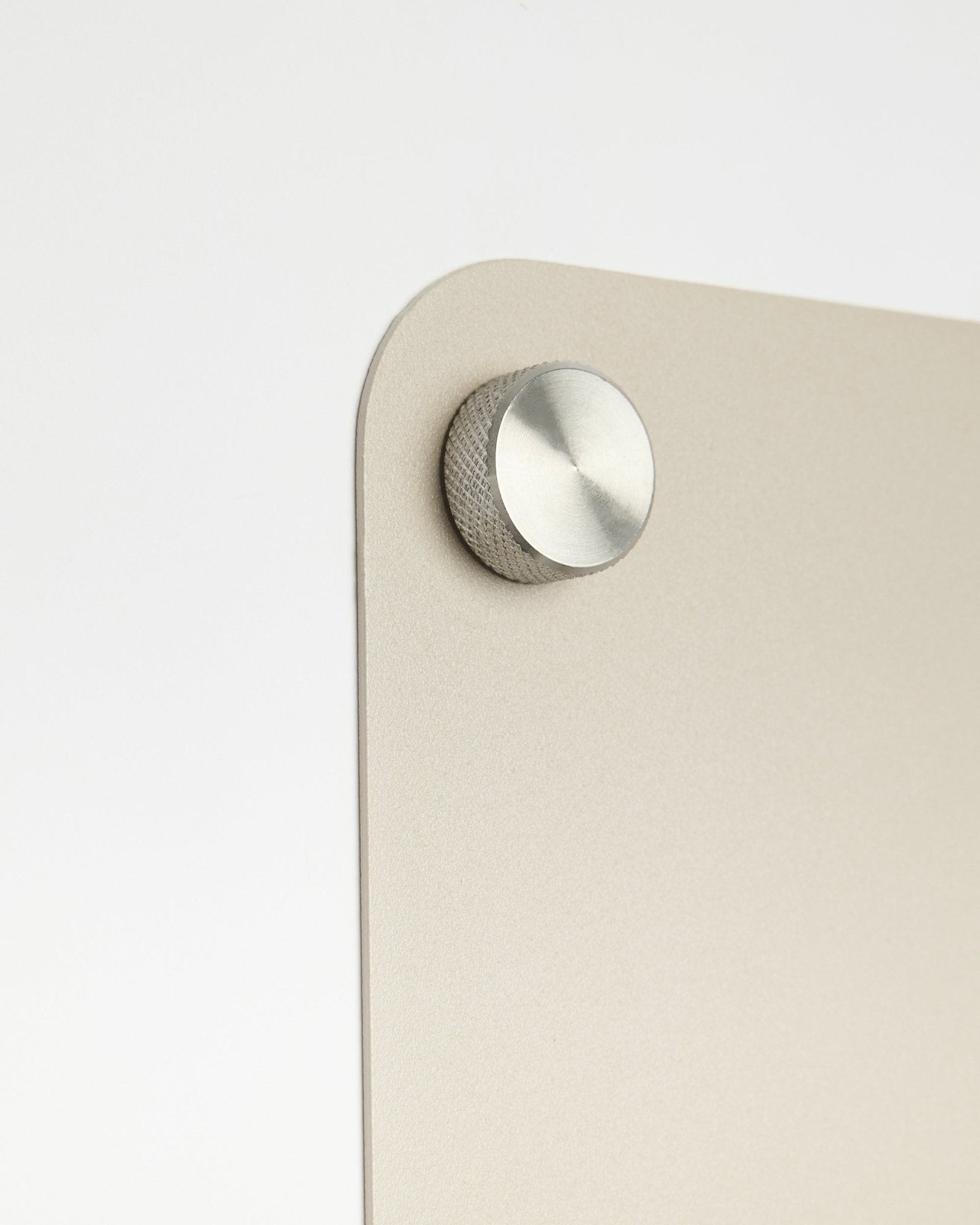 Primer plano de un accesorio de pomo redondo de metal fijado al tablero magnético large beige Norr de WoodUpp, con detalle de cristal esmerilado sobre fondo blanco.