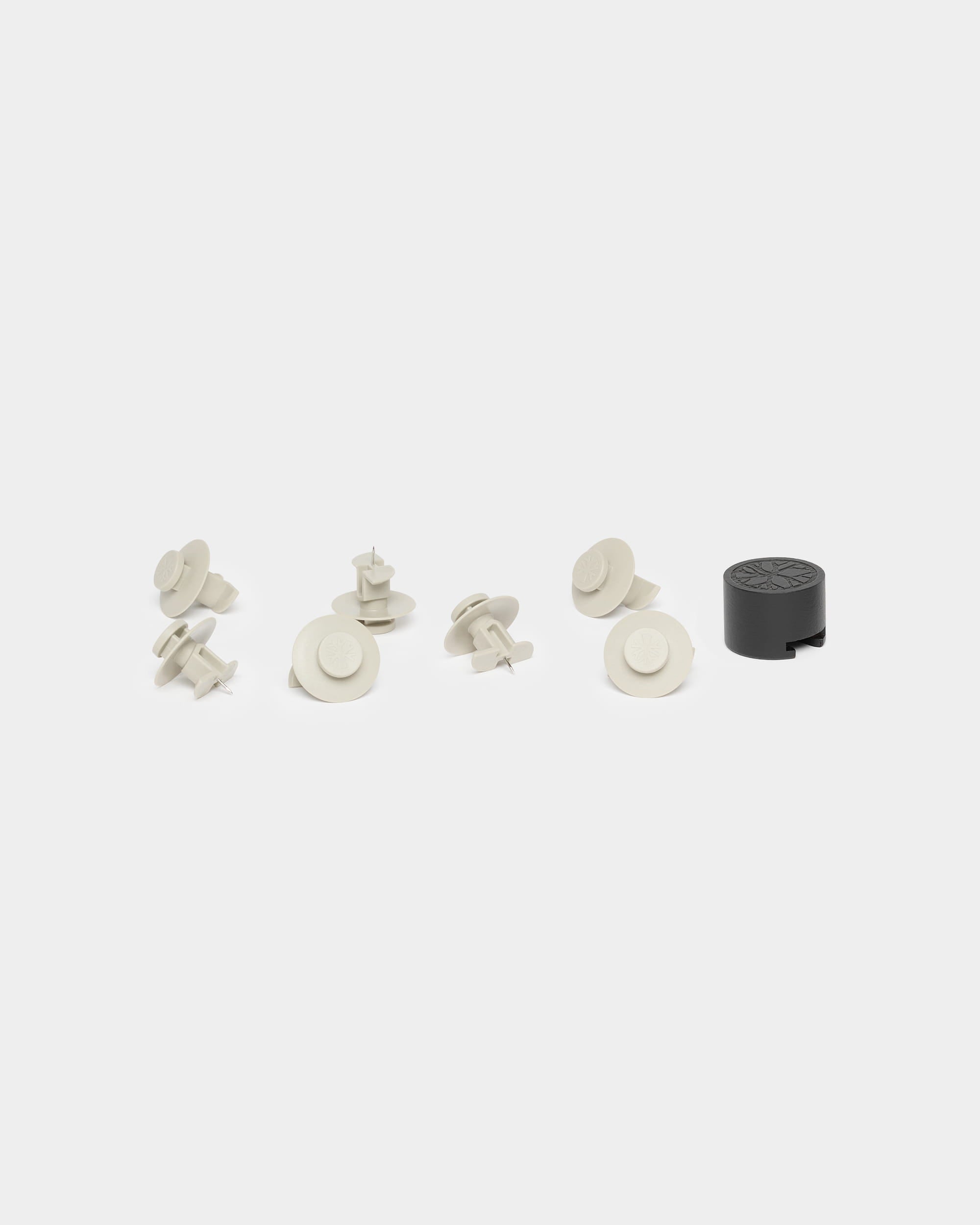 Siete fijaciones de color beige y una herramienta de instalación negra para WoodUpp Akupanel, expuestas sobre un fondo blanco.