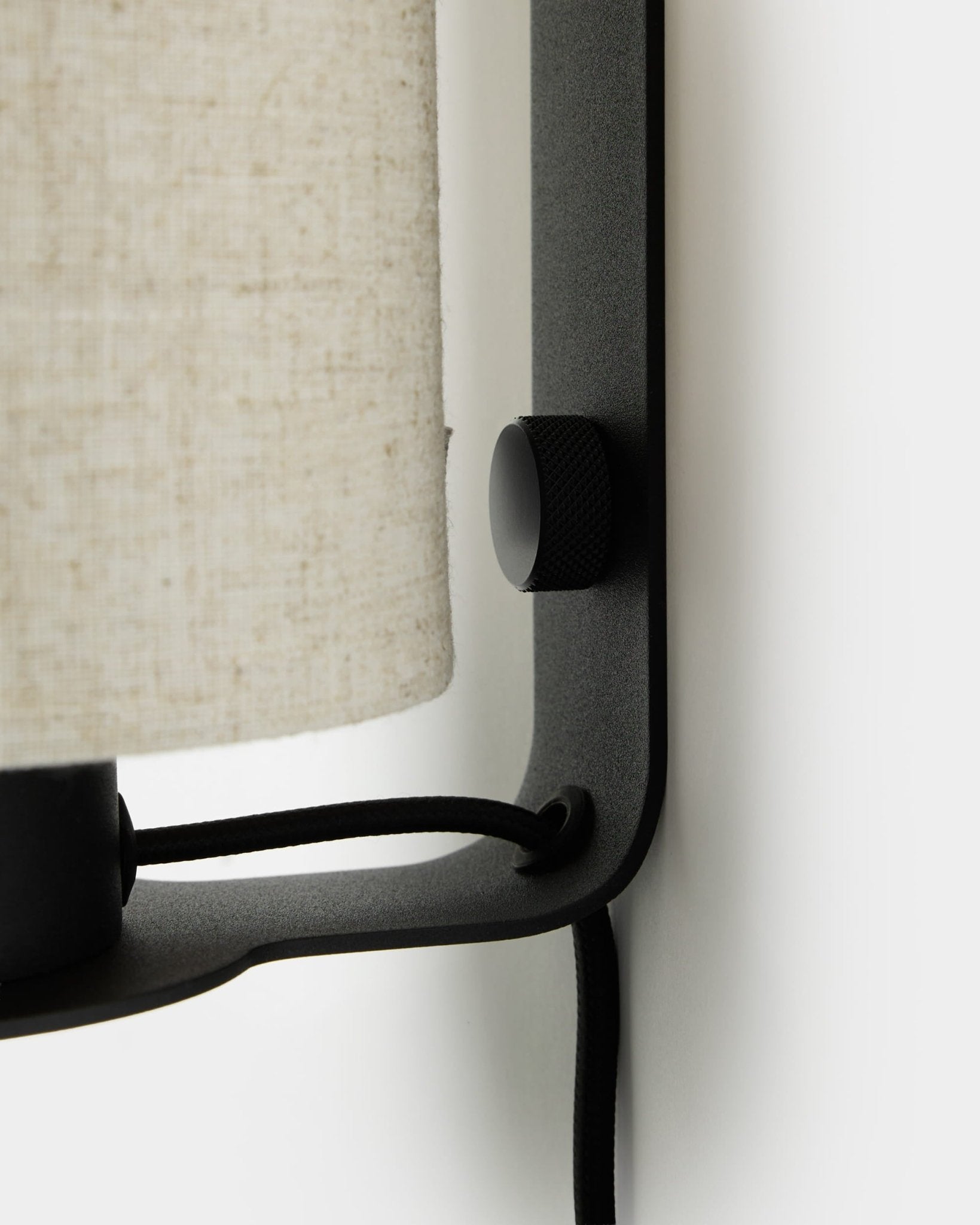 Primer plano del aplique de pared Feya de WoodUpp en black y beige, con perilla texturizada, pantalla de lino y algodón, y cable visible, montado sobre una pared blanca.