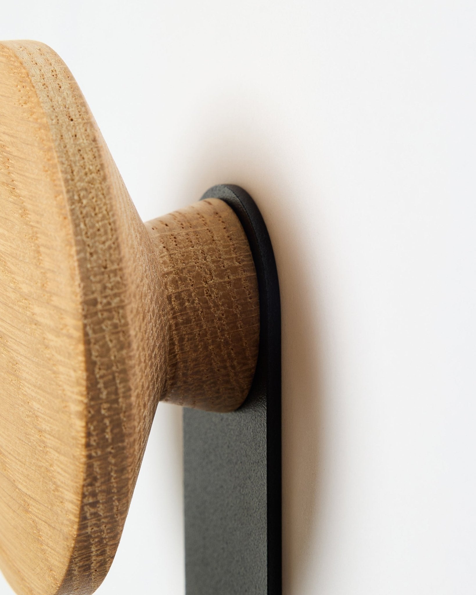 Primer plano del colgador Linn Vertical en natural oak de WoodUpp, un accesorio con pomo redondo de madera montado sobre un soporte black, diseñado para paneles acústicos Akupanel.