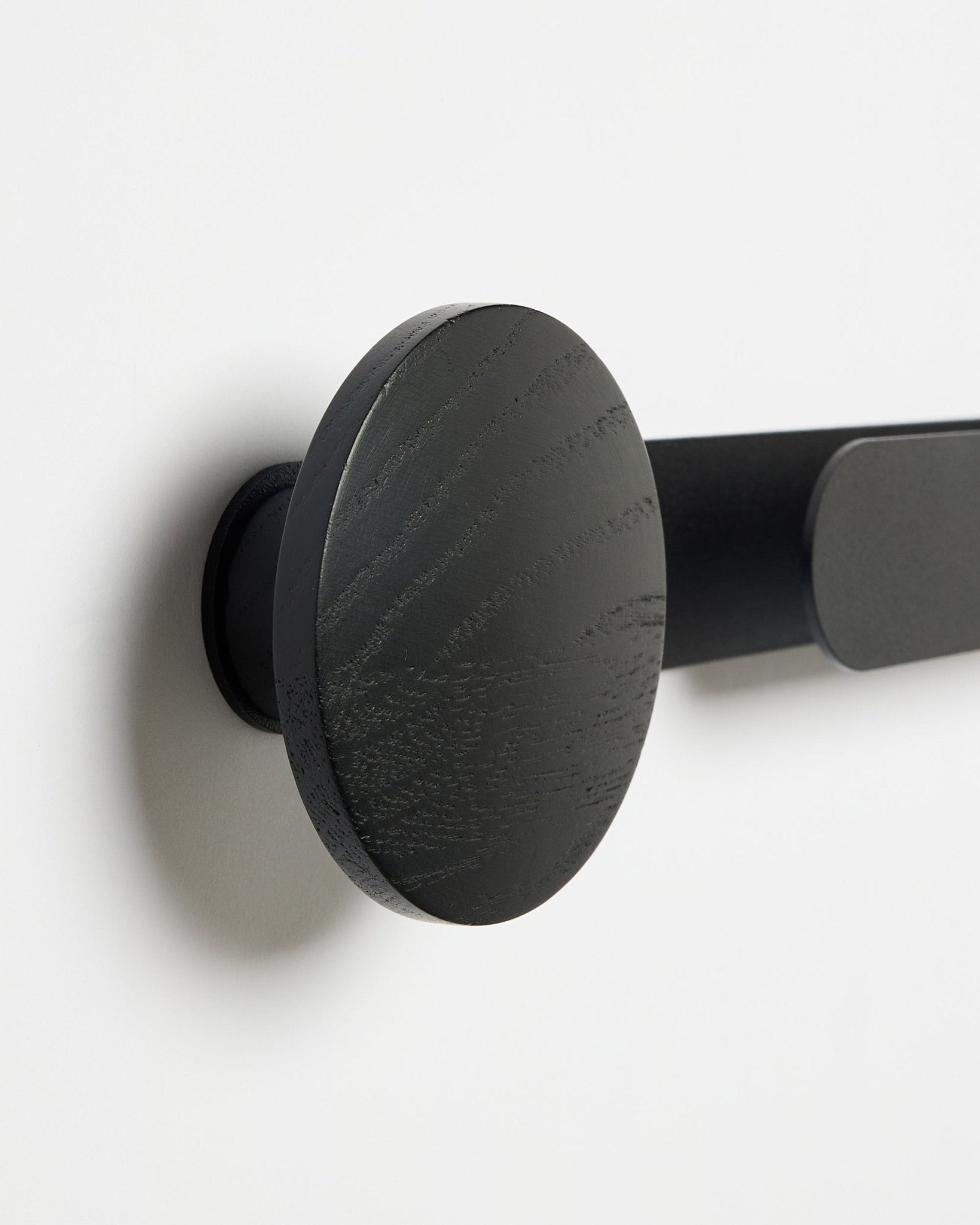 Primer plano del perchero WoodUpp Linn | Horizontal en Black Oak, acabado mate black, montado en una pared blanca; accesorio para paneles acústicos de madera.