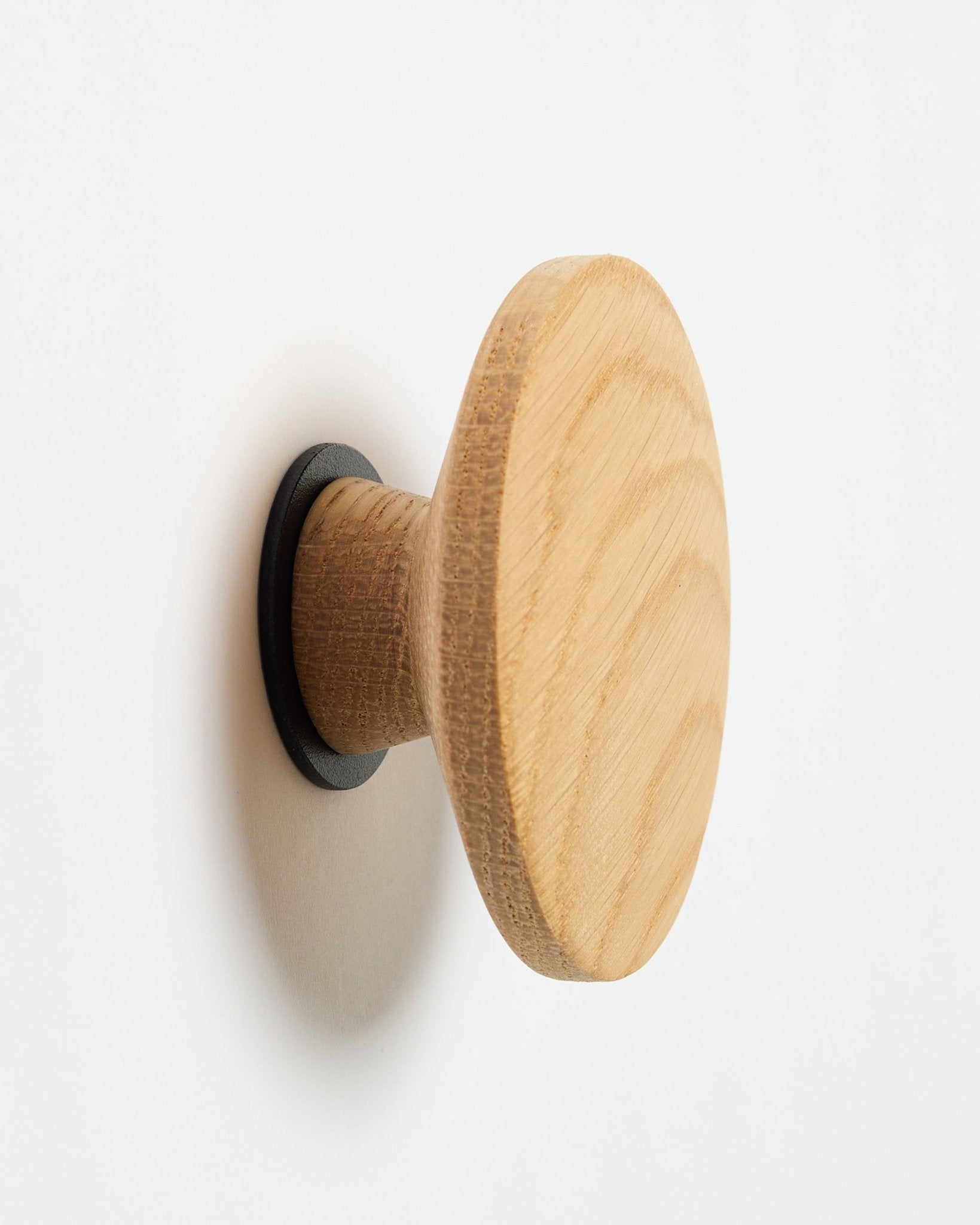 WoodUpp Linn I Single Hanger en natural oak, un colgador de pared redondo con base de black, diseñado como accesorio para montar en paneles acústicos de madera Akupanel.