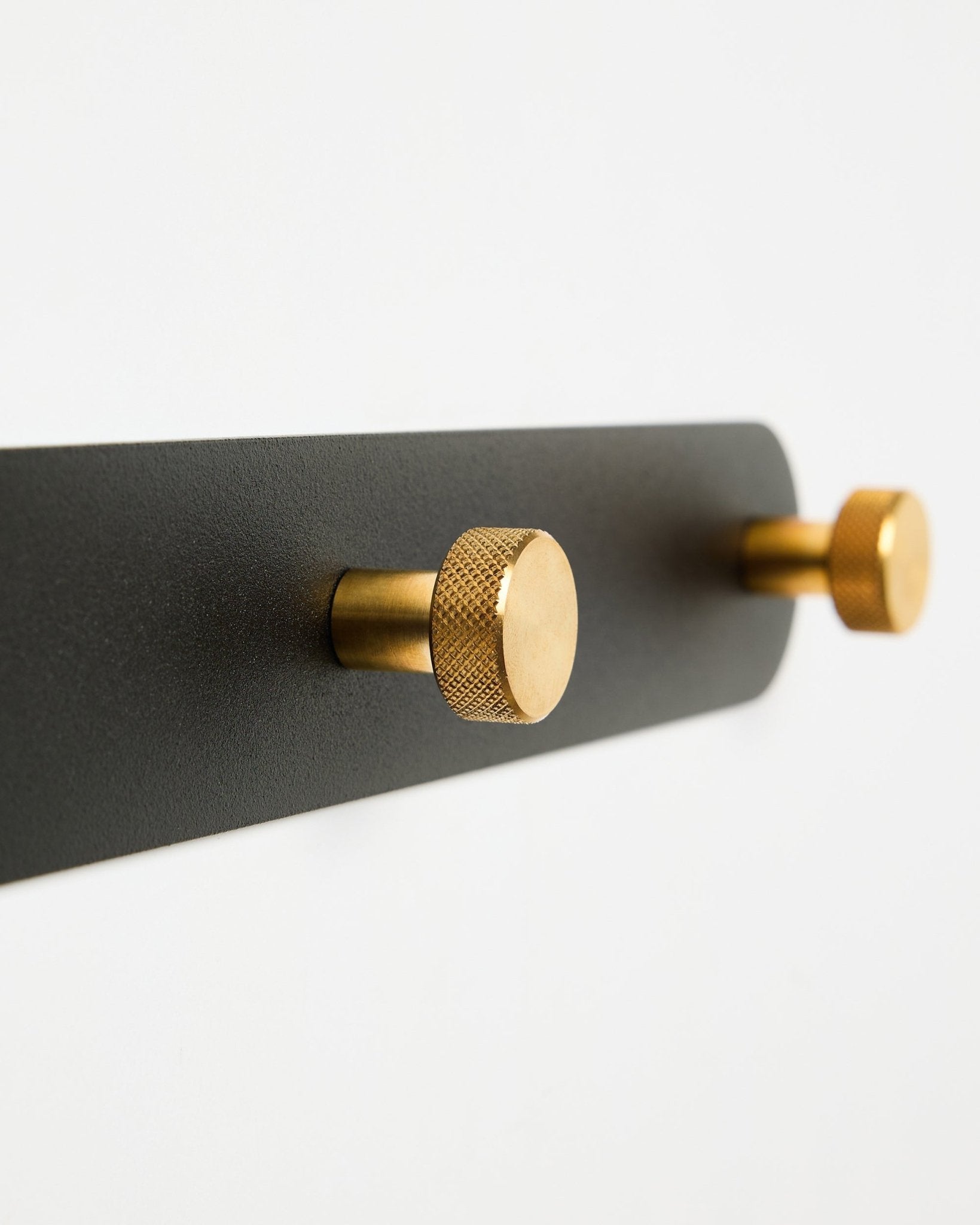WoodUpp Norr Coat Hook Rack, modelo X7, con dos ganchos cilíndricos black y brass sobre un soporte black, presentado sobre fondo blanco.