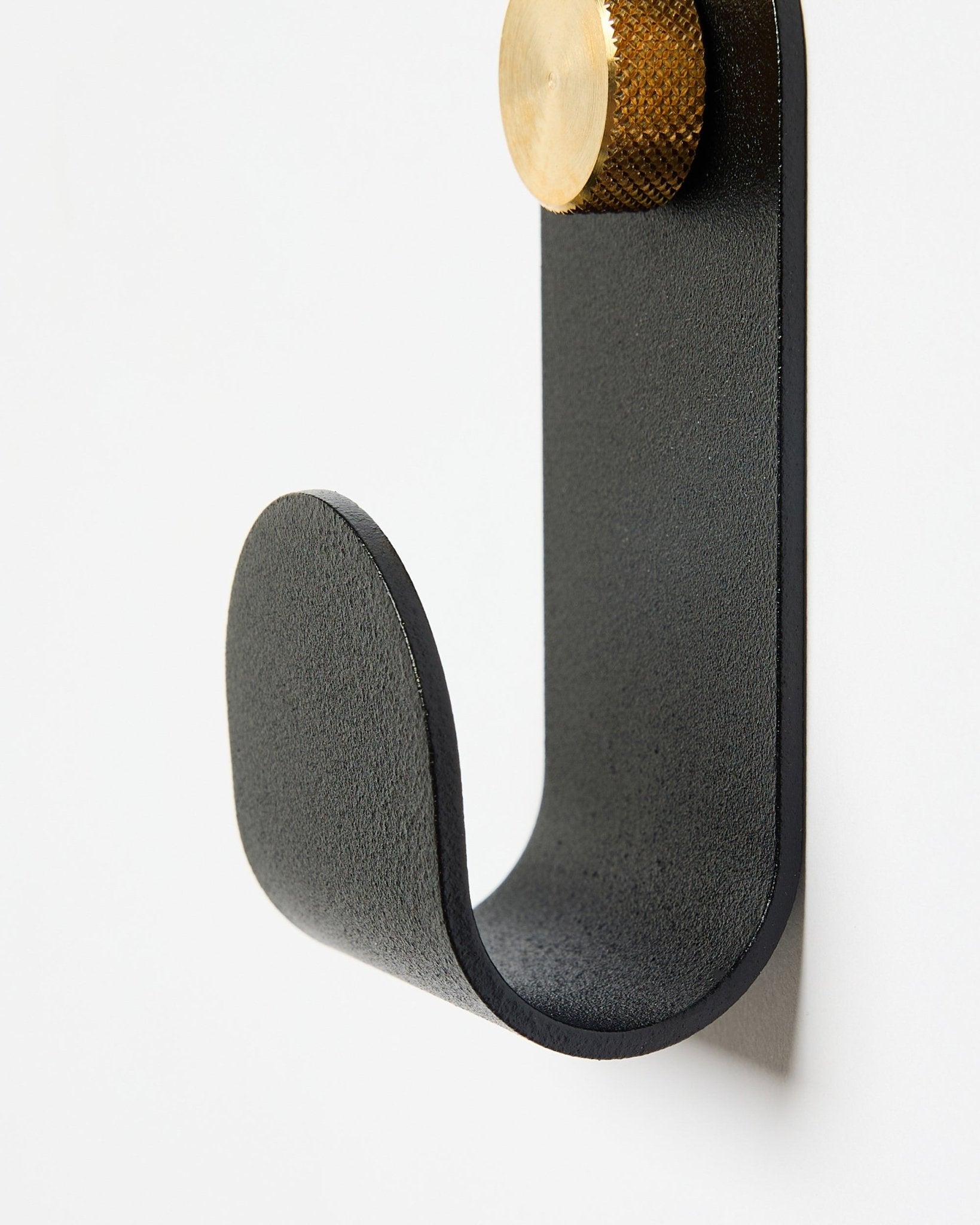 El Norr Single Hanger de WoodUpp tiene un brazo curvo de metal en black con un remate dorado, diseñado como accesorio para usar con paneles acústicos en paredes blancas.