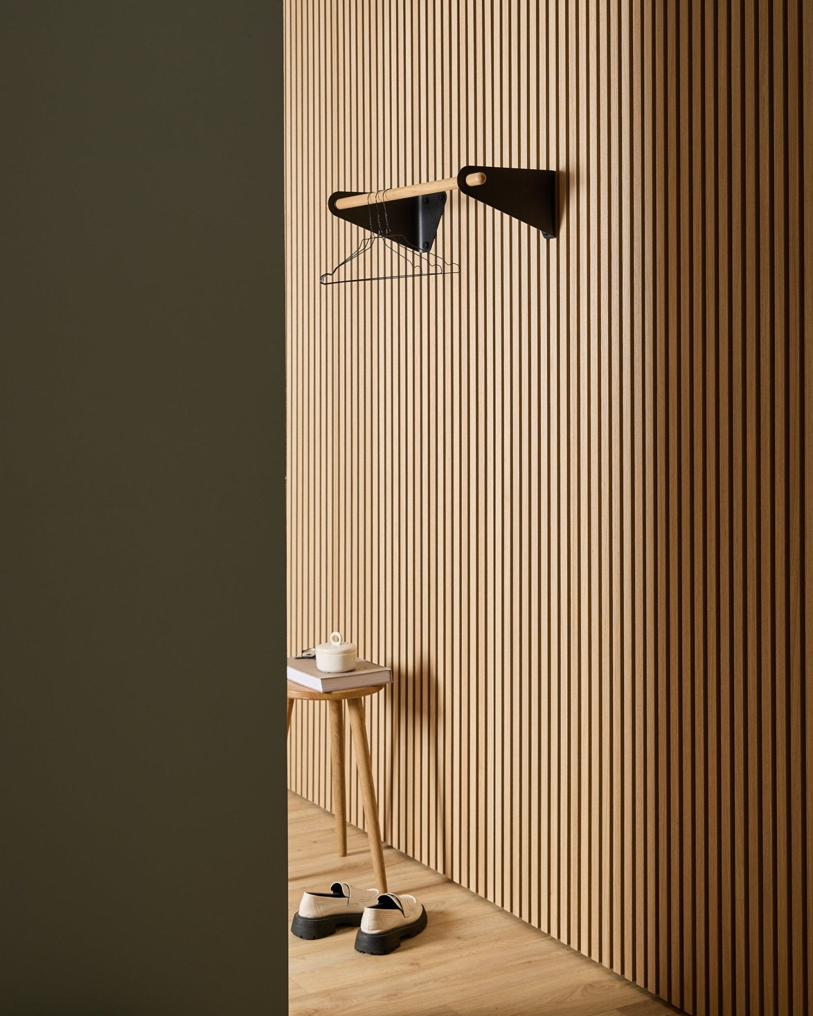 Entrada minimalista con paneles acústicos nórdicos de listones de madera WoodUpp Akupanel, perchero black Linn (75,9 cm), taburete, zapatos, estante de pared y rollo de papel.