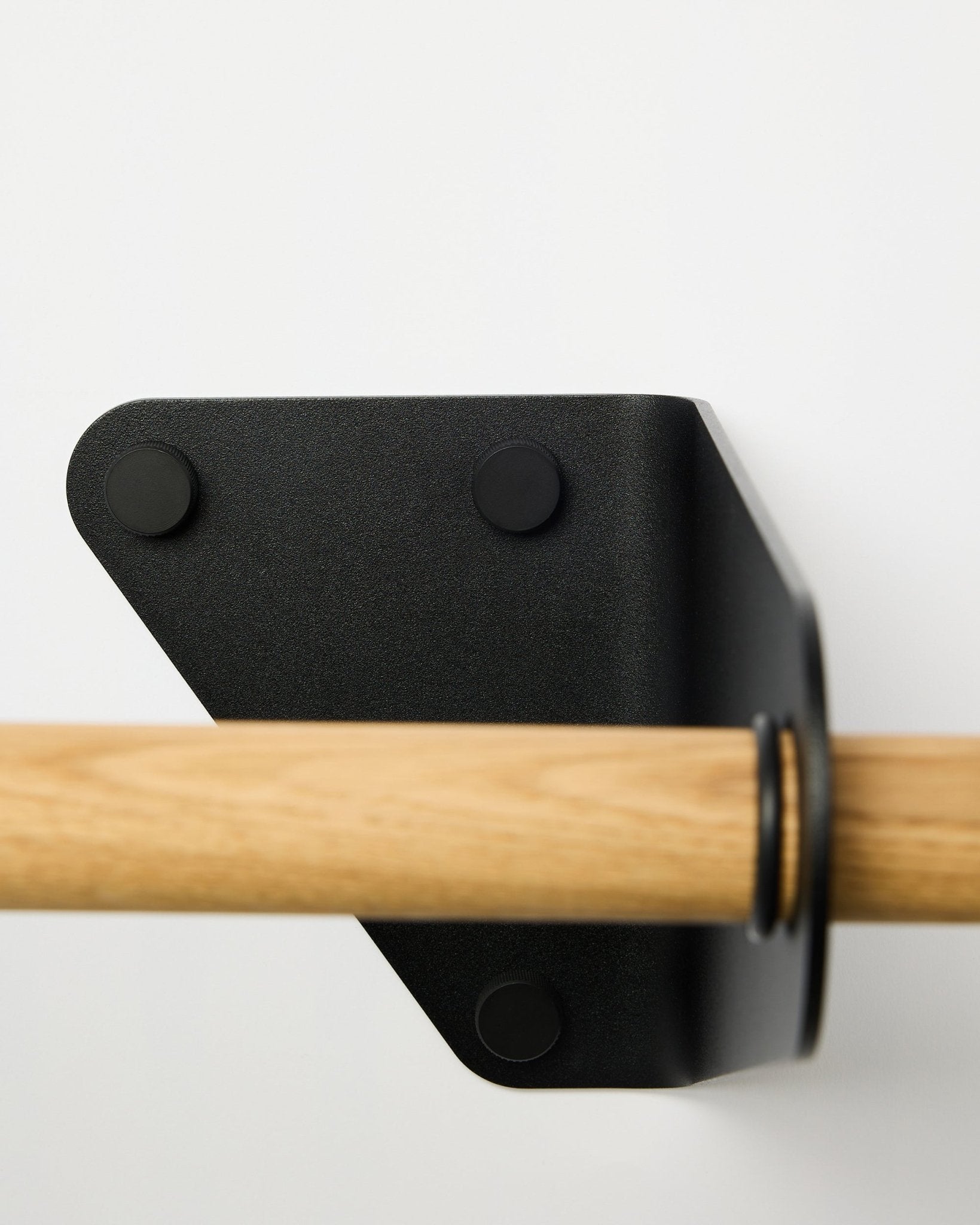 Primer plano del perchero Linn de WoodUpp en black, 115,9 cm, instalado en una pared blanca con un soporte metálico triangular, mostrado como parte de los accesorios acústicos nórdicos.