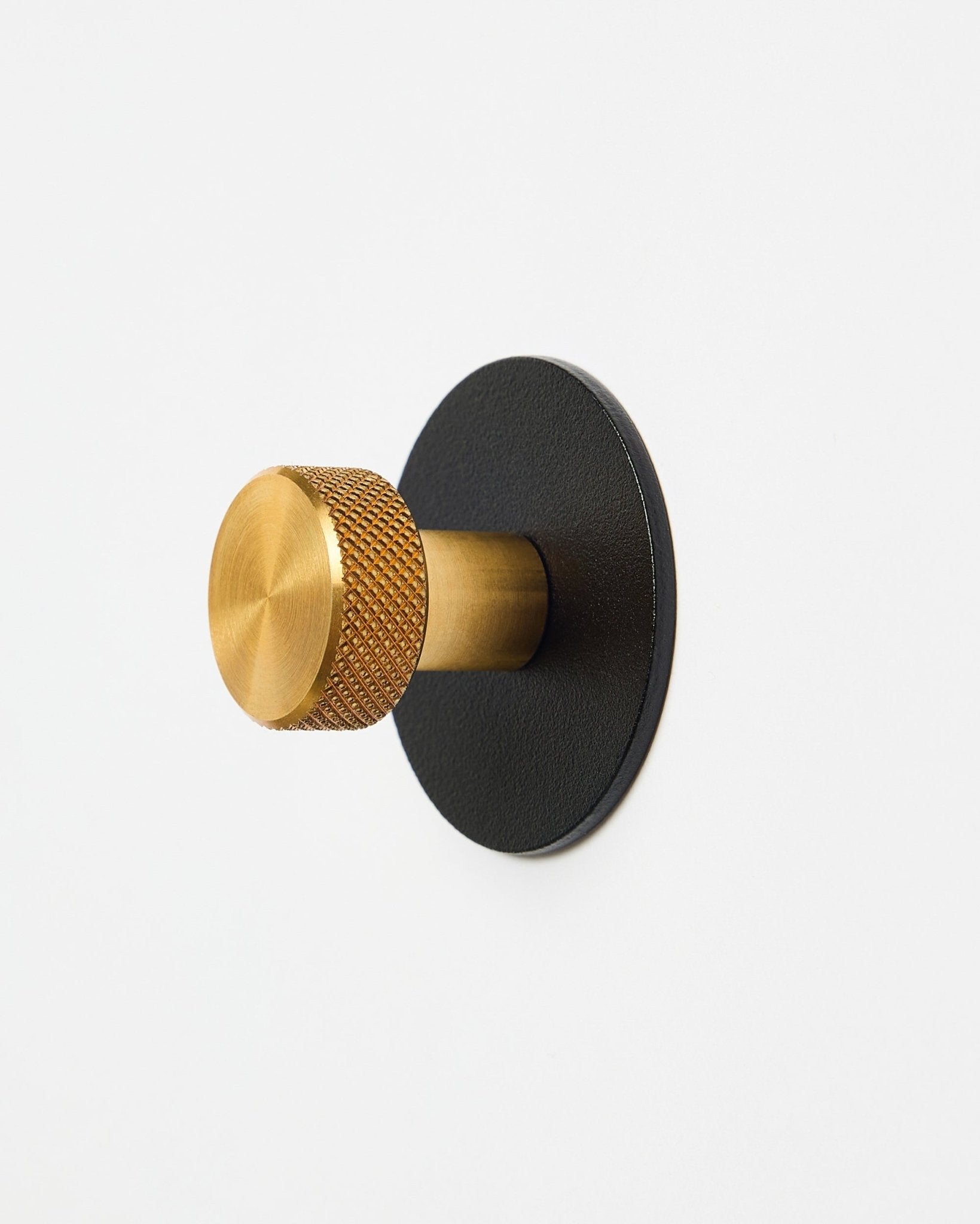 Percha Norr Coat Hook X1 de WoodUpp con pomo texturizado brass y base de steel con recubrimiento en polvo black, accesorio para Akupanel, presentada sobre fondo blanco.