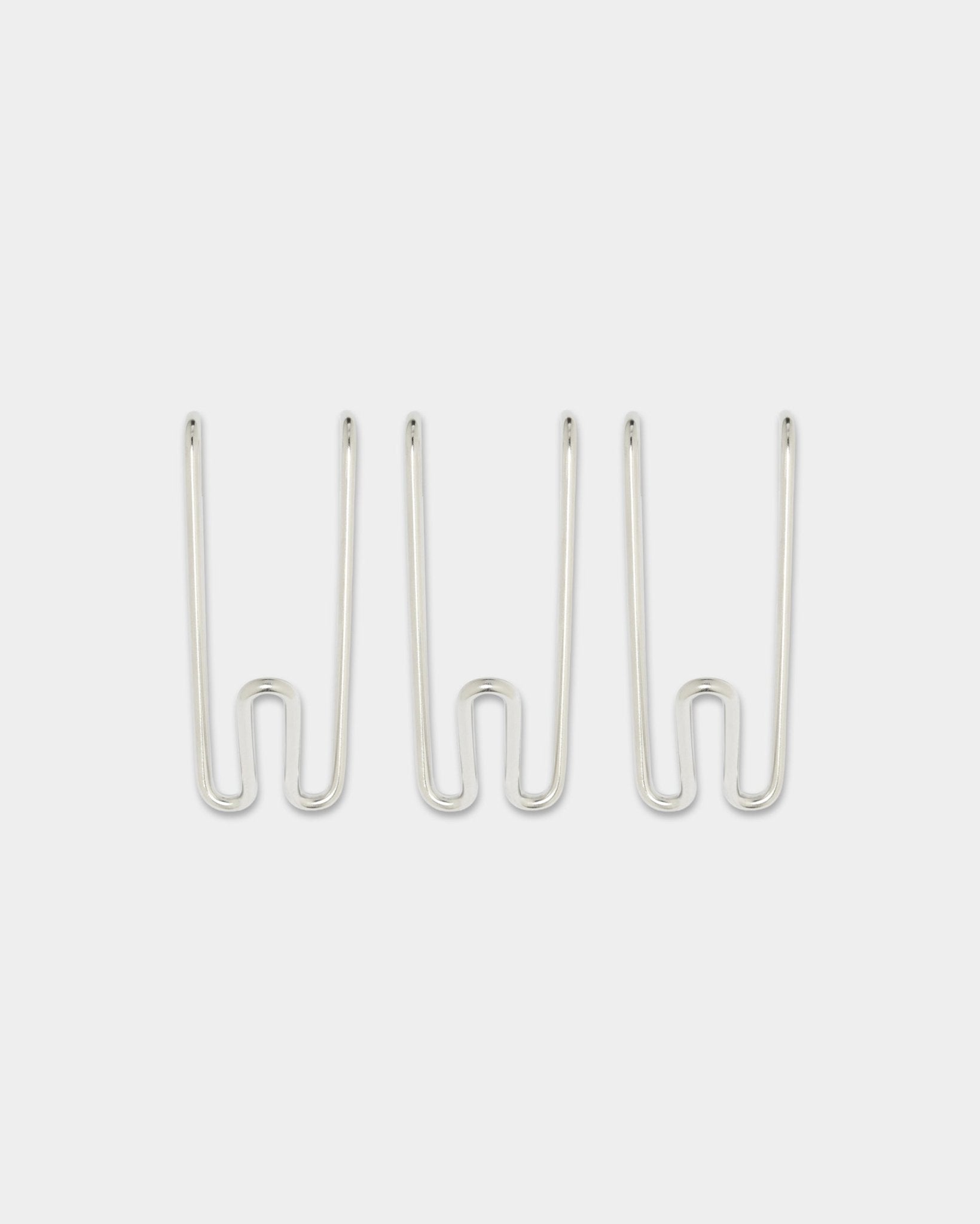 Tres ganchos Alva Wire Hook BM1, cortos, en acero inoxidable steel de la colección CREATE de WoodUpp, colocados a la misma distancia sobre un fondo blanco liso.