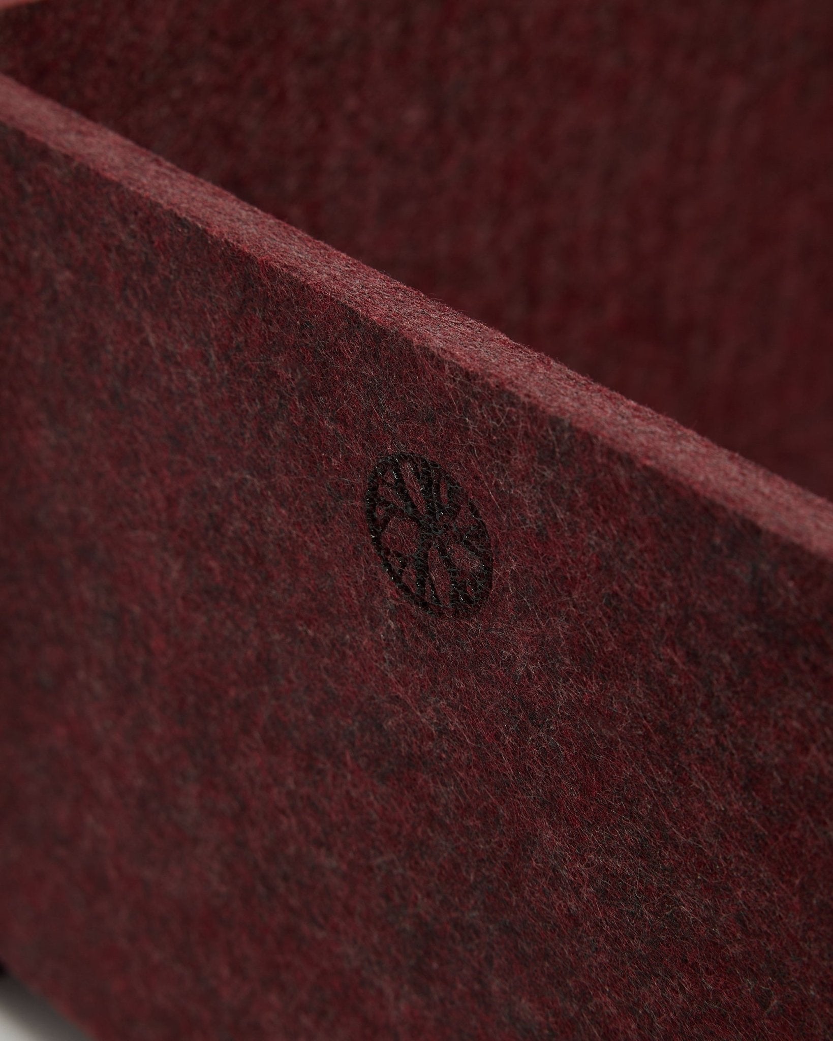 Primer plano de WoodUpp Vigg | Felt Box / BM2 en ox red, que muestra fieltro PET texturizado y un emblema circular black en la esquina. Diseño de accesorio acústico nórdico.