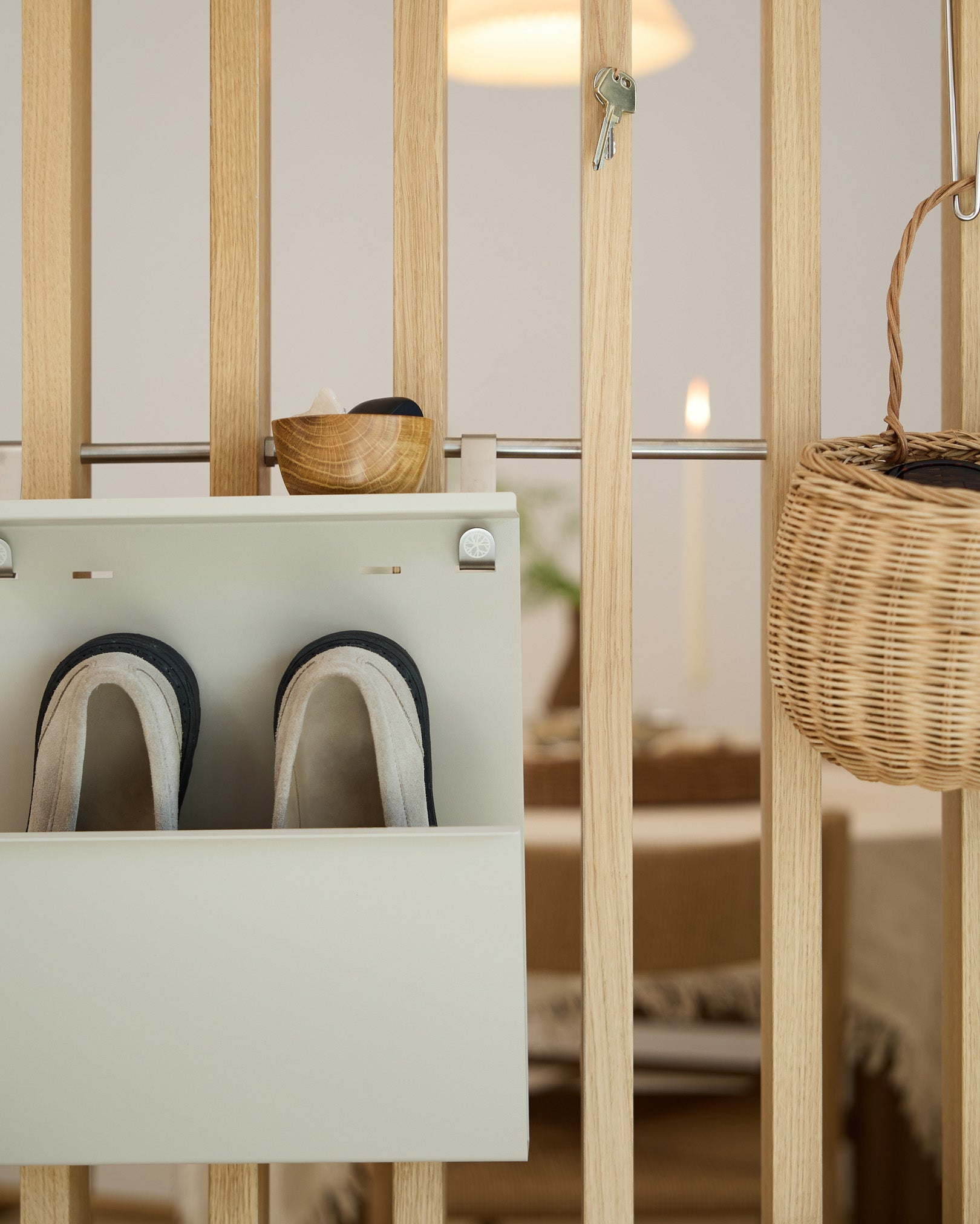 WoodUpp Nell Beige Shoe Storage muestra zapatillas, un cuenco y una cesta de mimbre sobre un separador de ambientes de madera; al fondo se ve la zona de comedor.