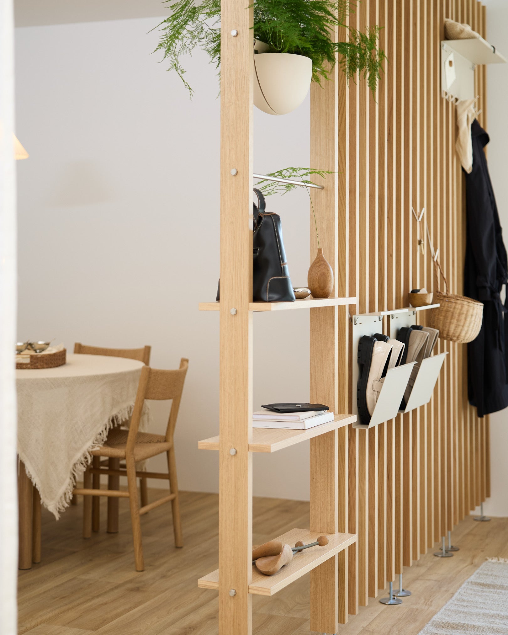 Una estantería abierta de madera divide la zona de comedor e incorpora Nell Shoe Storage en beige de WoodUpp para mantener los zapatos organizados en un hogar nórdico moderno.