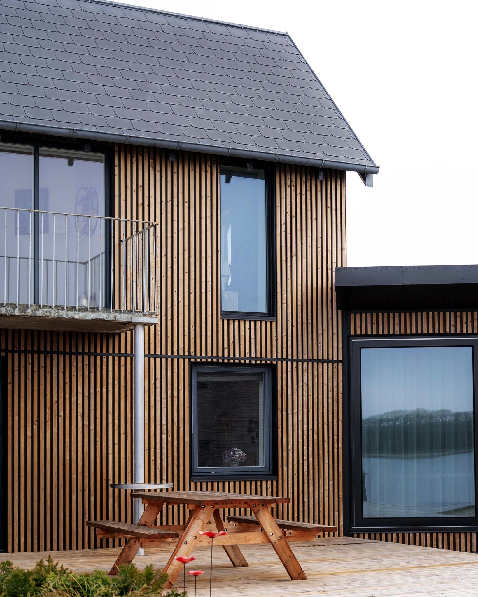 Casa moderna con paneles de fachada WoodUpp Aluwood en Brown aceitado, con ventanas large, un balcón y una terraza con mesa de pícnic de madera.