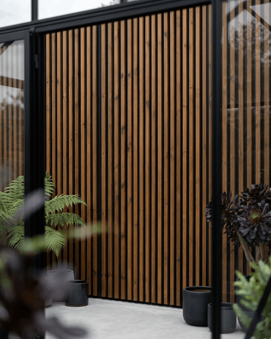 Panel de fachada exterior WoodUpp Aluwood en brown aceitado, combinado con jardineras black y plantas verdes, creando un entorno de patio nórdico minimalista.