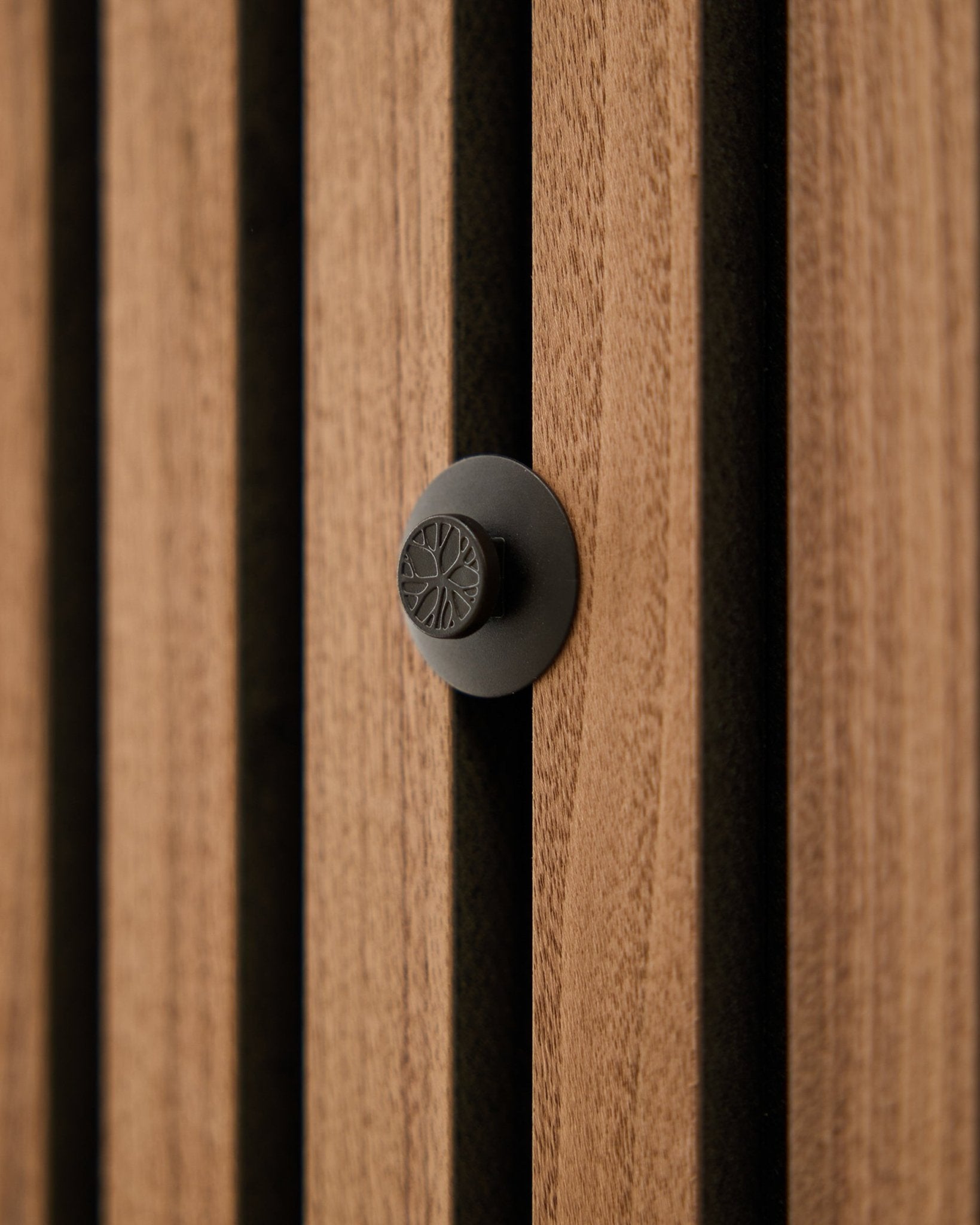 Primer plano de un pomo redondo black del set Original WoodUpp Dupps, instalado en una pared acústica moderna de lamas de madera vertical Akupanel.