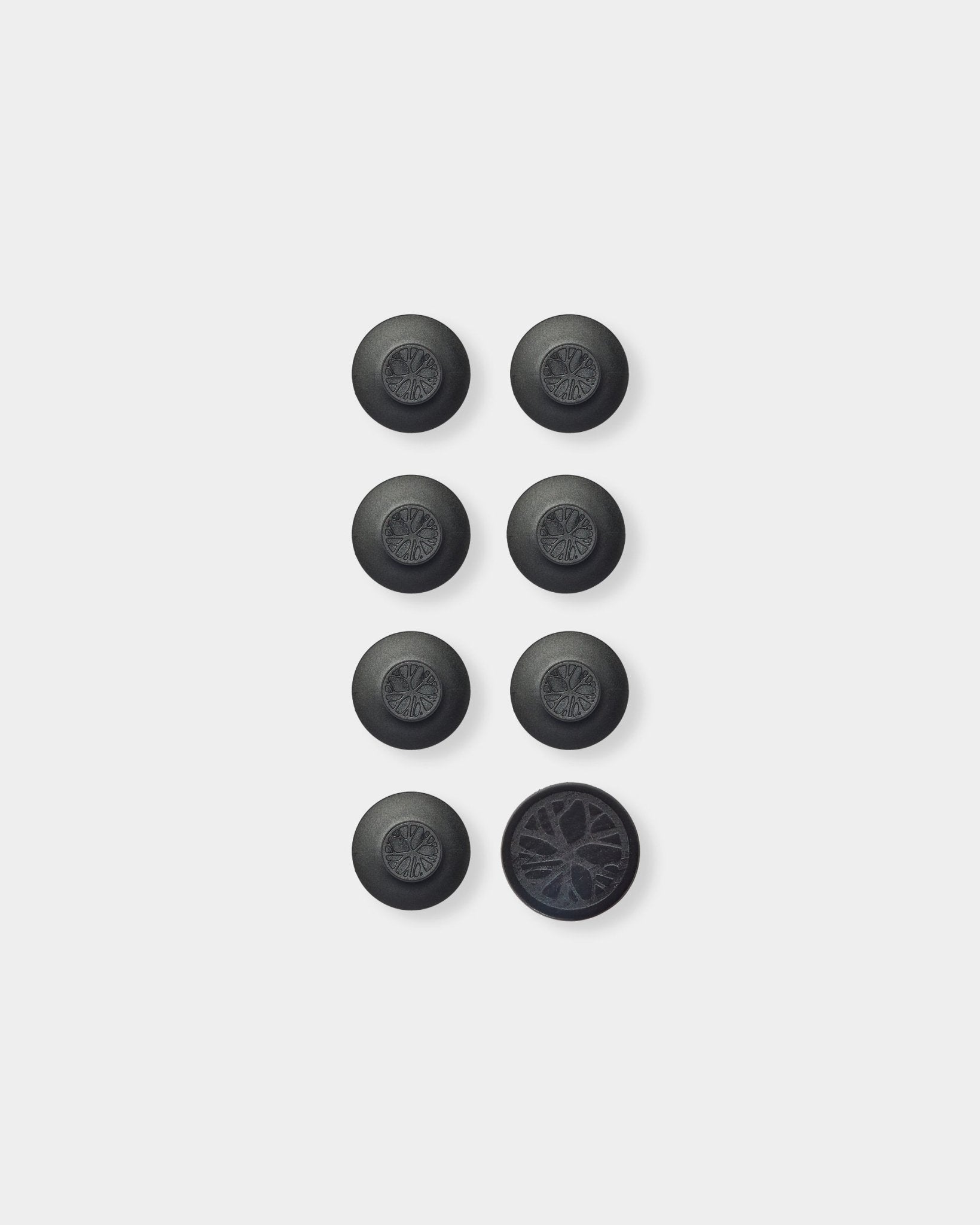 Siete accesorios redondos black Dupps Panel acústico de WoodUpp y una herramienta, colocados en una cuadrícula; abajo a la derecha, Dupp está volteado para mostrar su reverso texturizado.