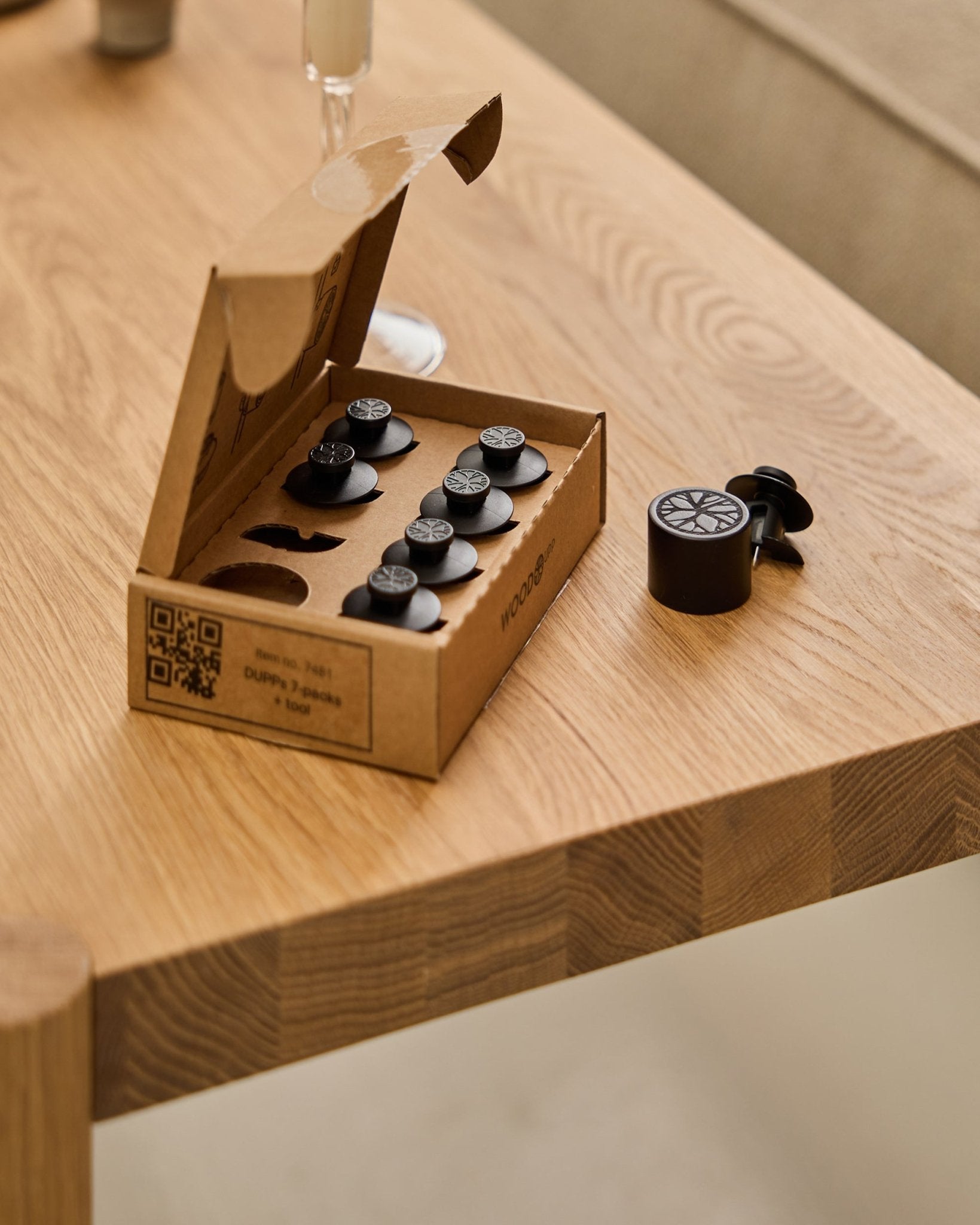 El set WoodUpp Dupps Original (7 piezas y 1 herramienta) colocado sobre una mesa de madera, con una pieza Dupps y parte de un vaso visibles en el borde.