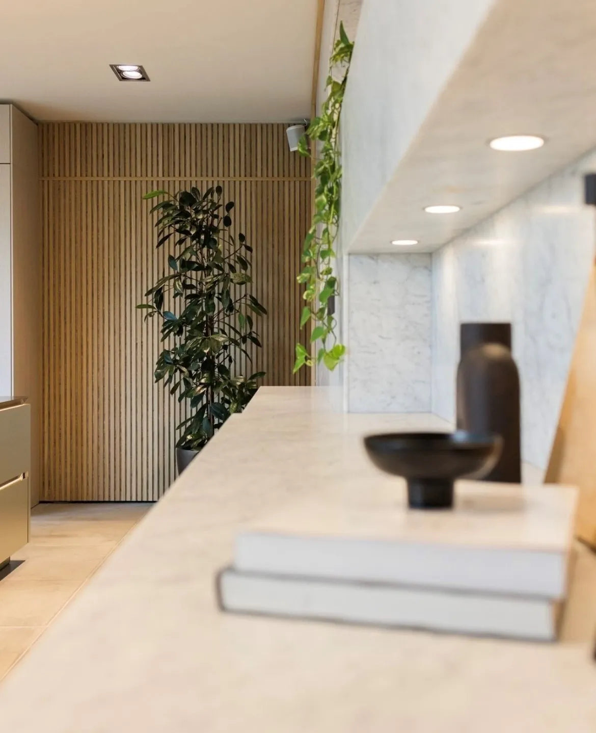 Un interior moderno con una estantería de mármol, objetos decorativos, plantas verdes y una pared de paneles de madera acústica nórdica Akupanel al fondo.