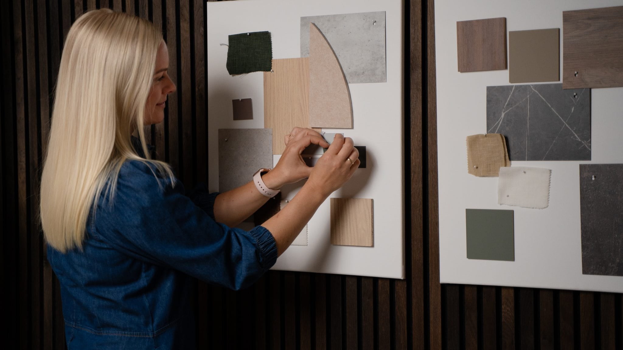 Una mujer ordena muestras de telas y colores en un tablero de inspiración, con otro tablero a su lado, cerca de paneles acústicos de madera de la colección Akupanel de WoodUpp.