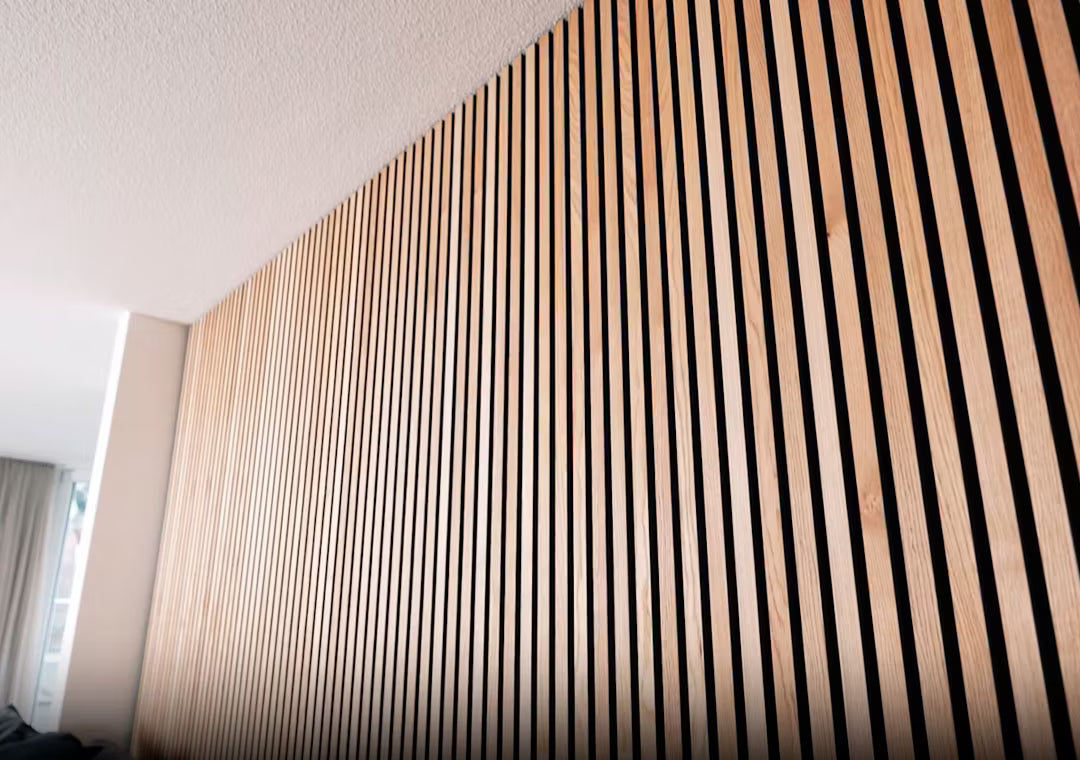 Detalle del panel acústico de madera Akupanel con lamas verticales de madera a rayas, instalado en una pared interior bajo un techo blanco.