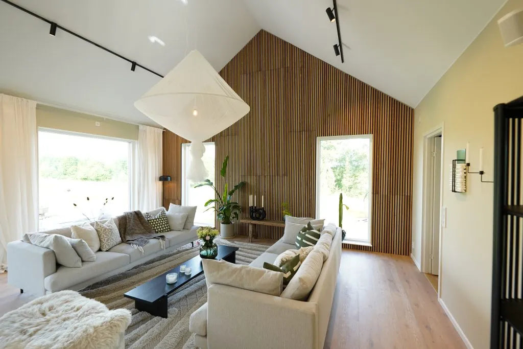 Moderno salón con techos altos, grandes ventanales, sofás luminosos, pared de acento de madera acústica Akupanel, plantas de interior y abundante luz natural.